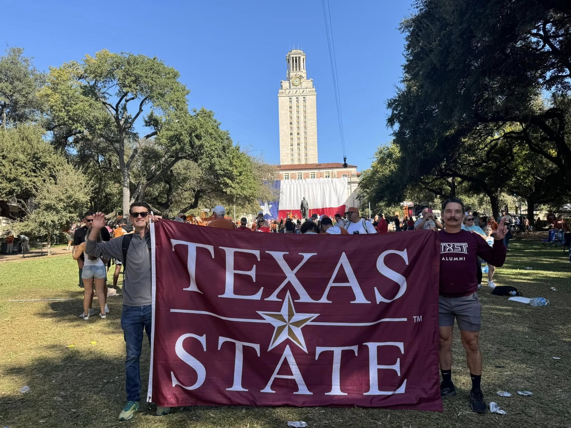 Two Texas State alums holding up a Texas State flag
