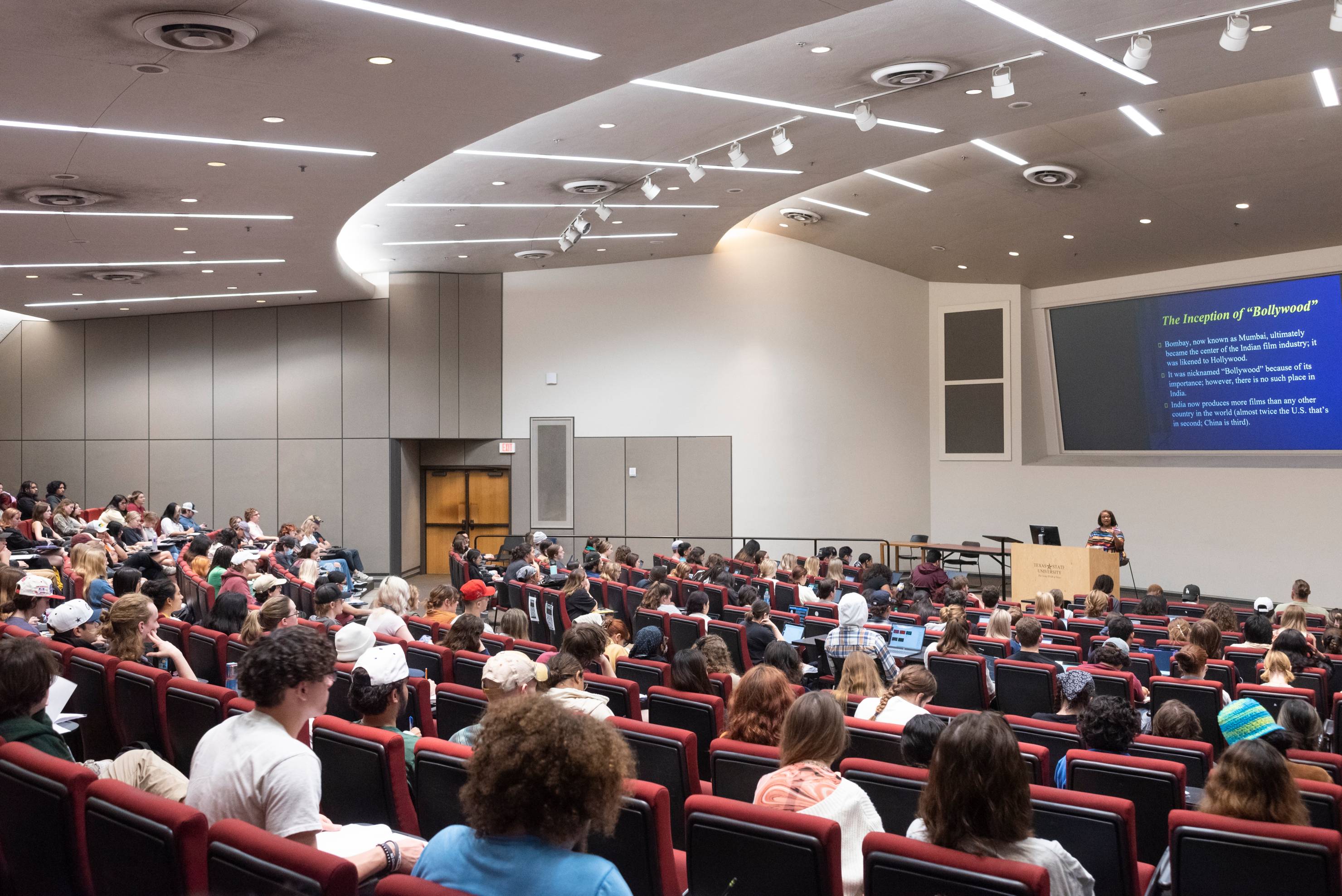 A large lecture hall is filled with students while a professor teaches.