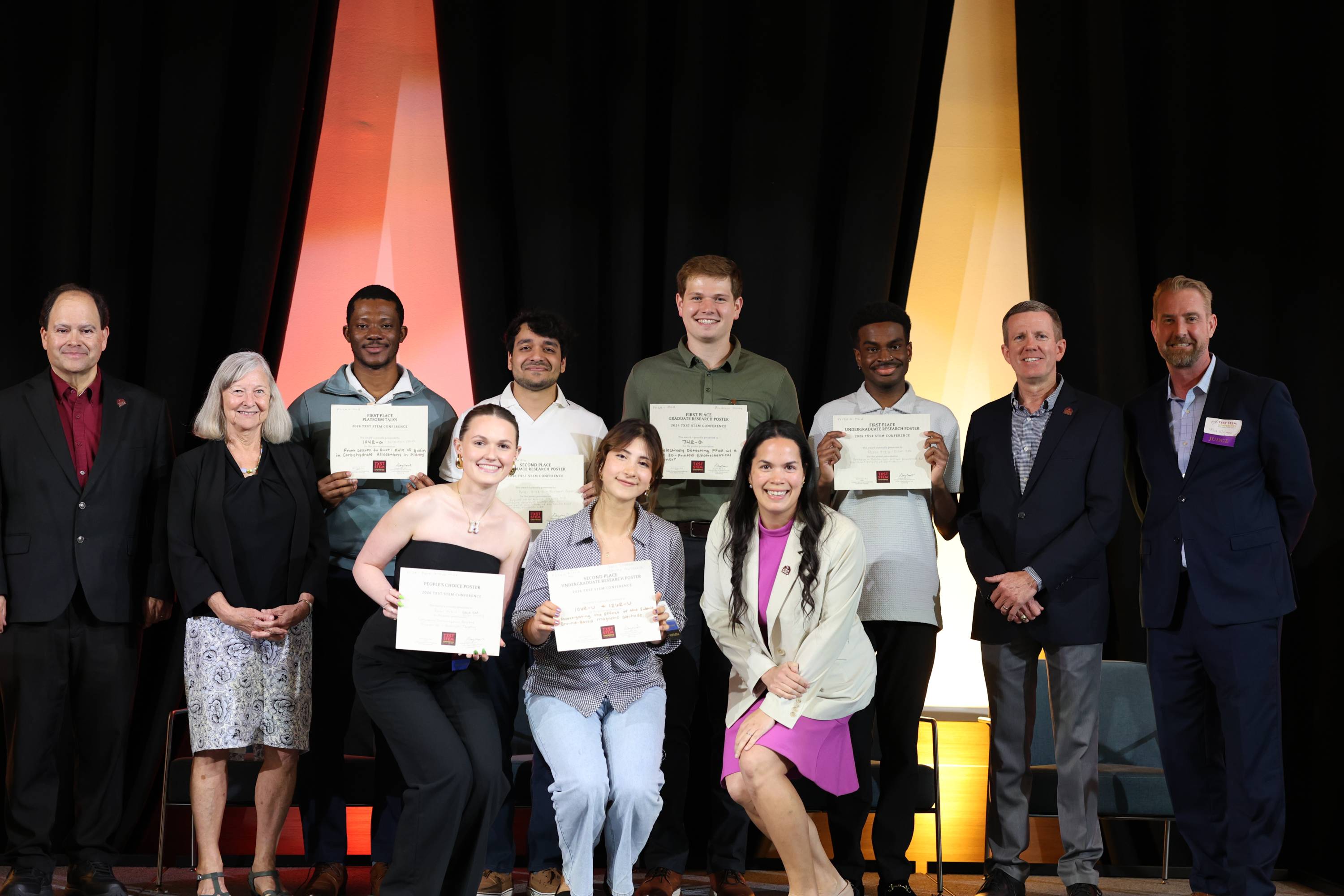 Ten award winners and organizers pose on a stage at the TXST STEM Conference, with several students holding certificates for first and second place research posters, platform talks, and the People's Choice Poster award.