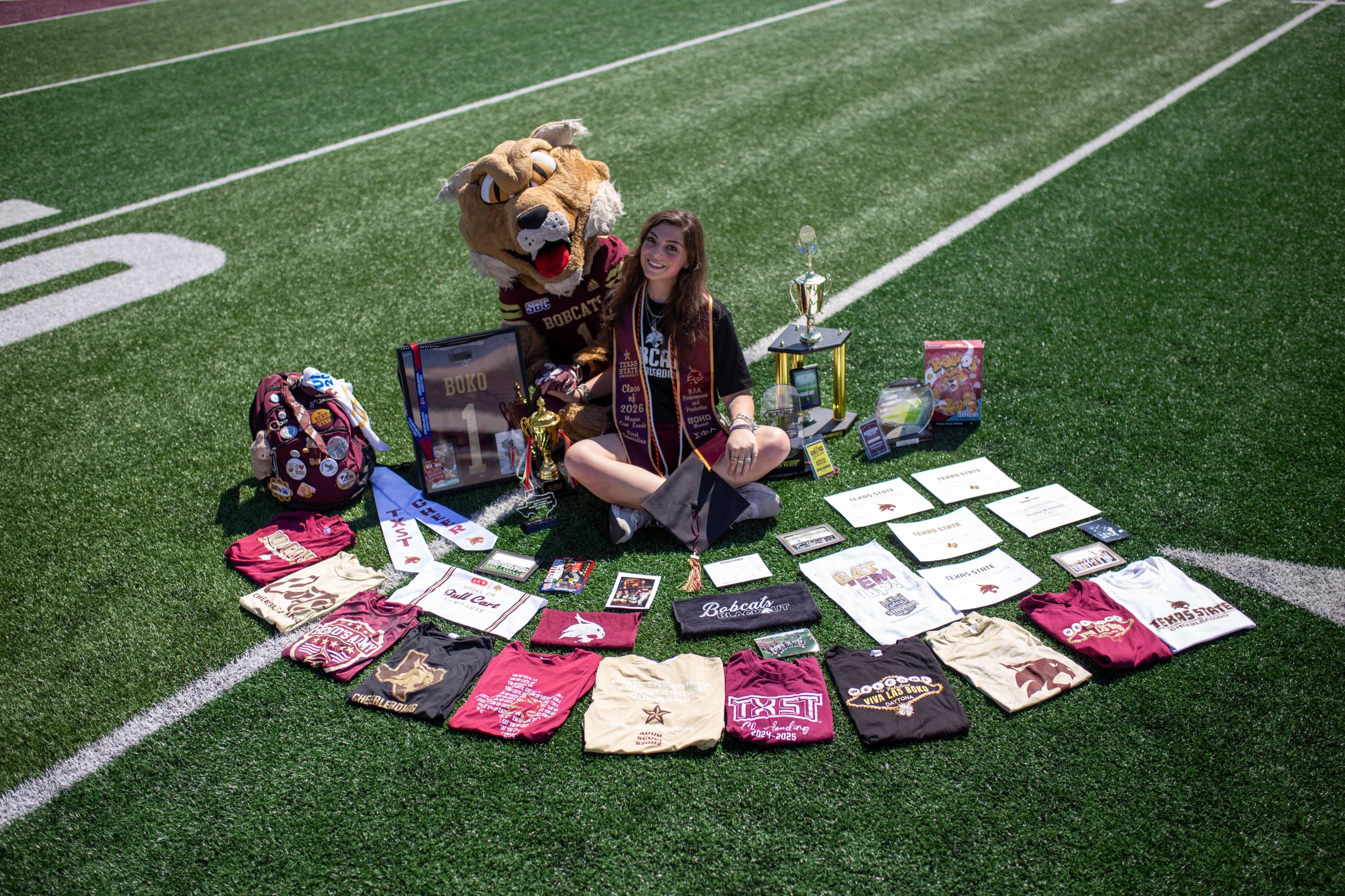 woman sitting on football field surrounded by txst memoriabilia and the bobcat mascot