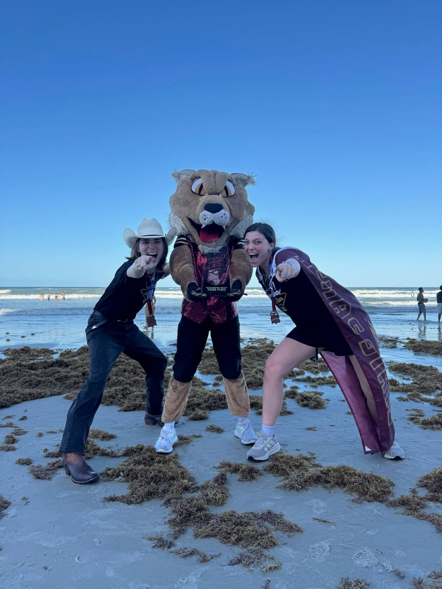 two women stand on either side of bobcat mascot and point at camera