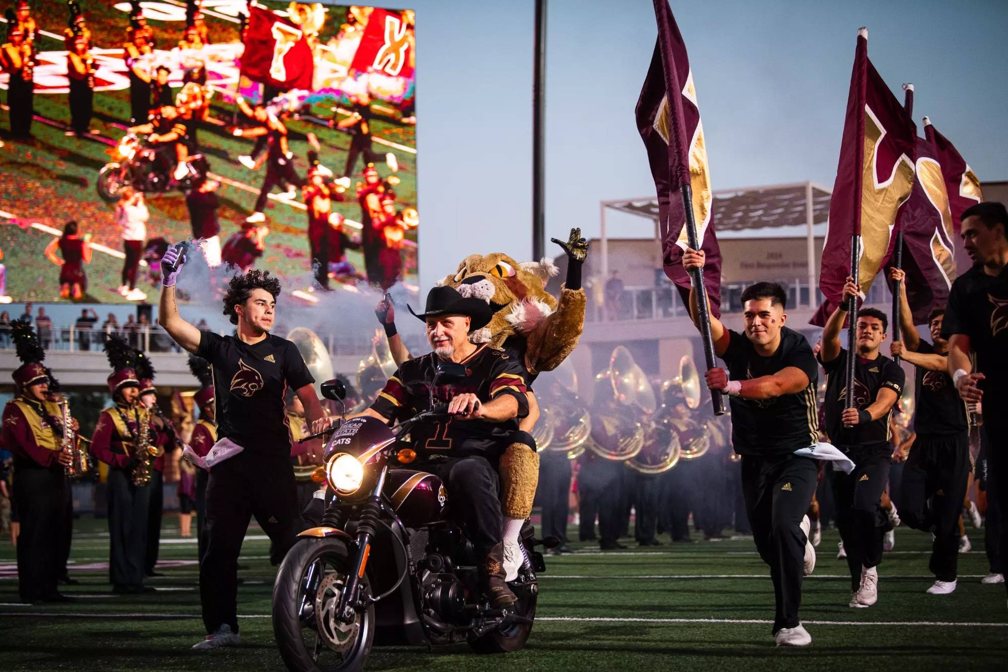 bobcat mascot riding on the back of a motorcycle as they drive into the football field during a game