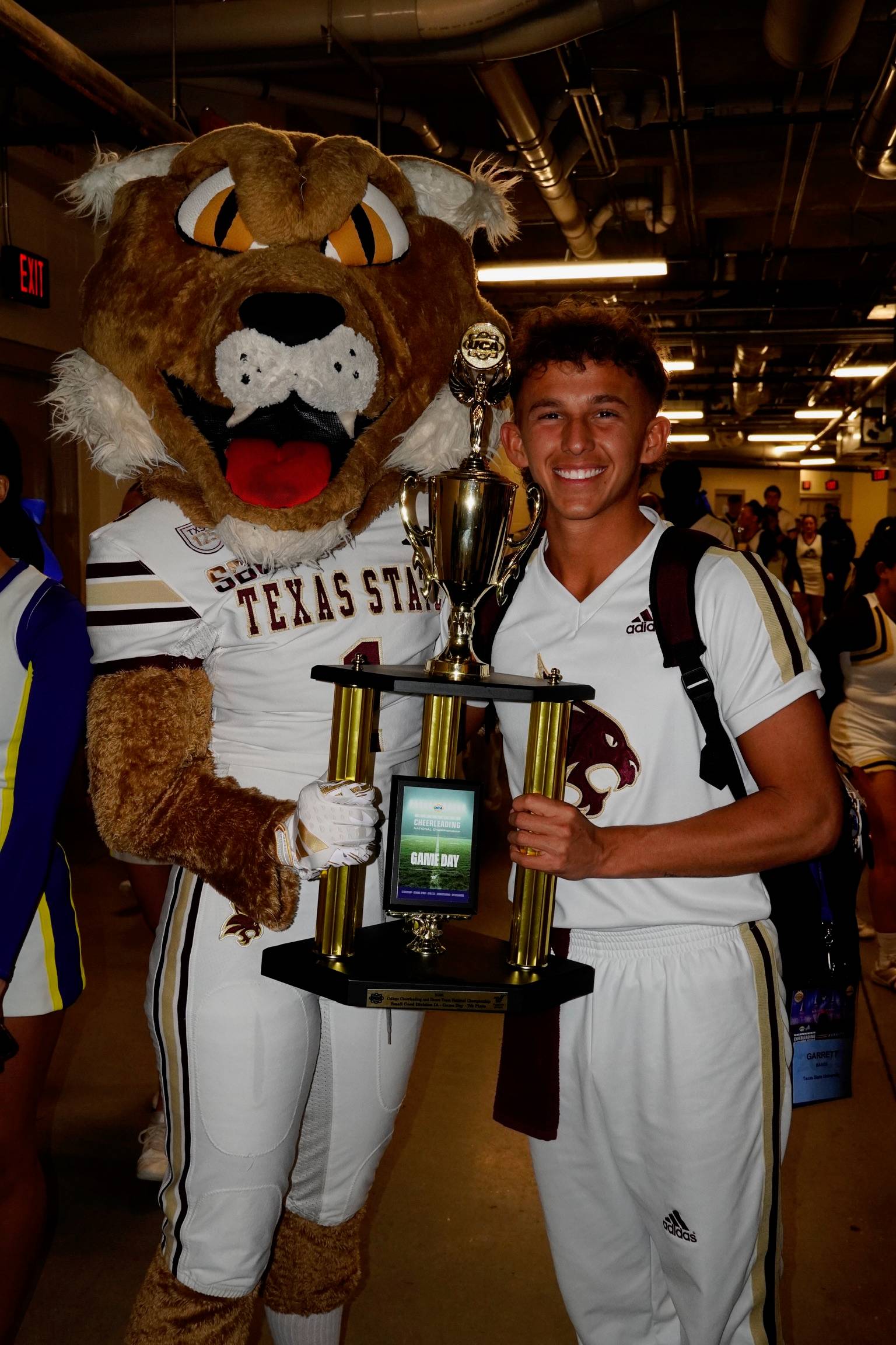 bobcat mascot and male cheerleader pose with trophy