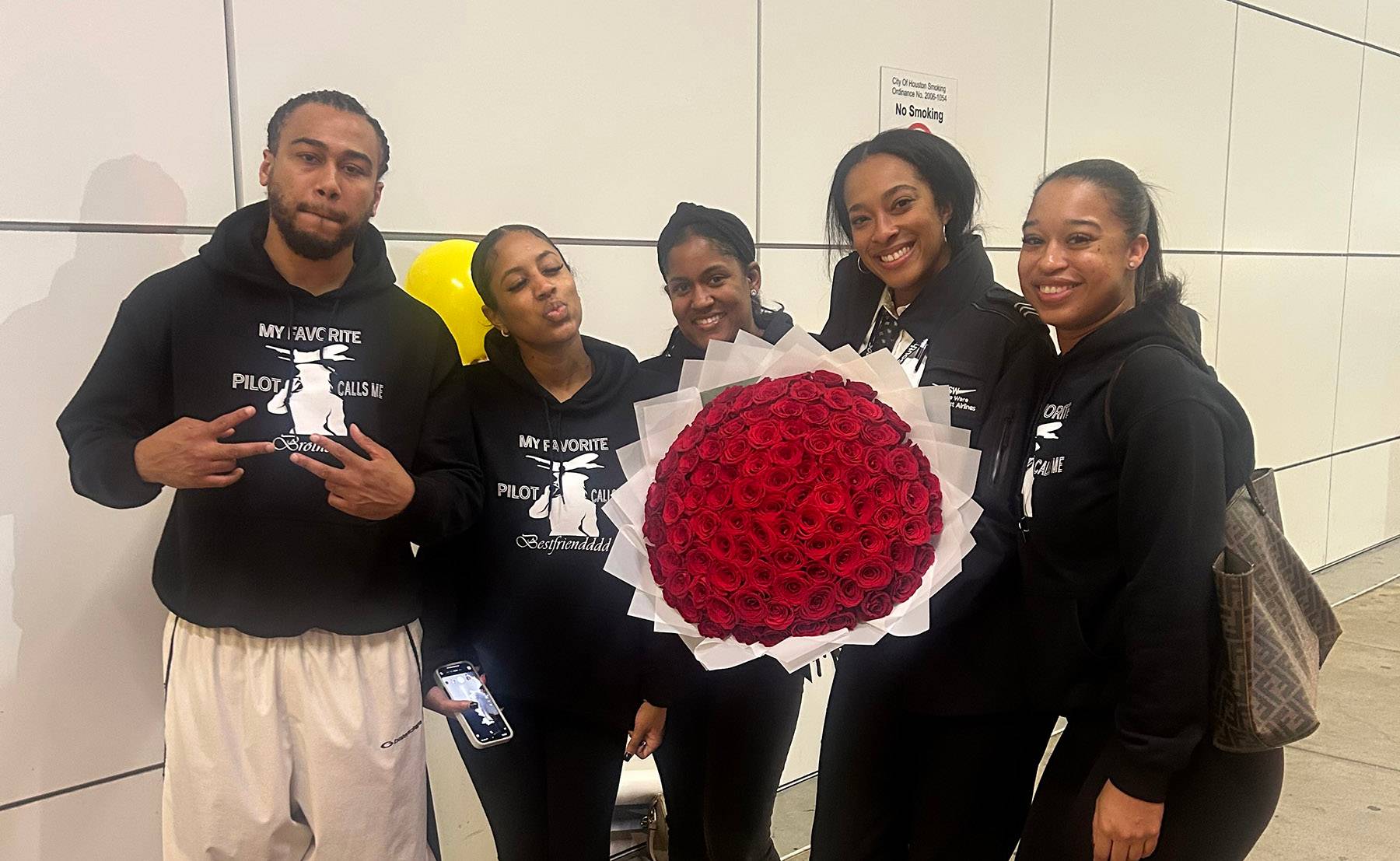 Five family members gathered together wearing matching black shirts. One of them is holding a large bouquet of roses. 