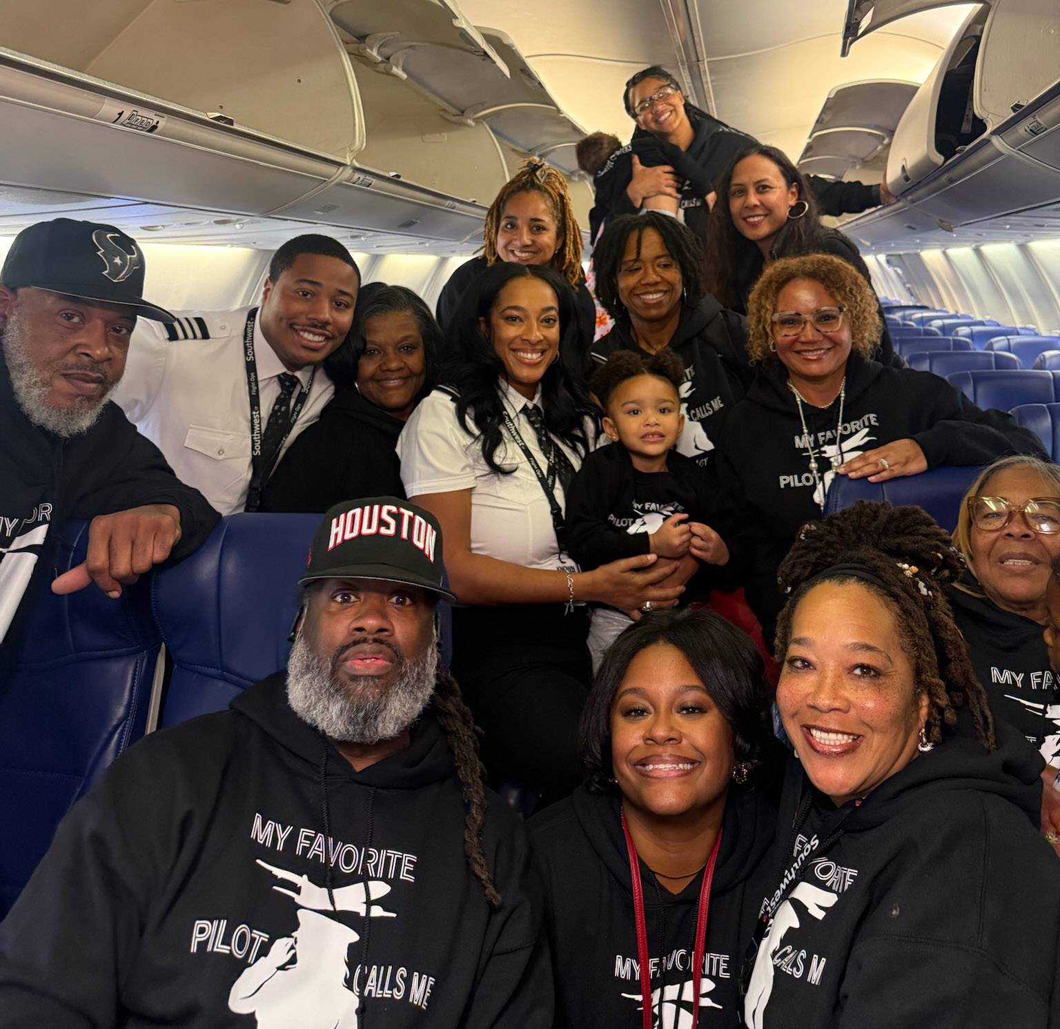 A large family gathered together in the cabin of an airplane wearing matching black shirts.