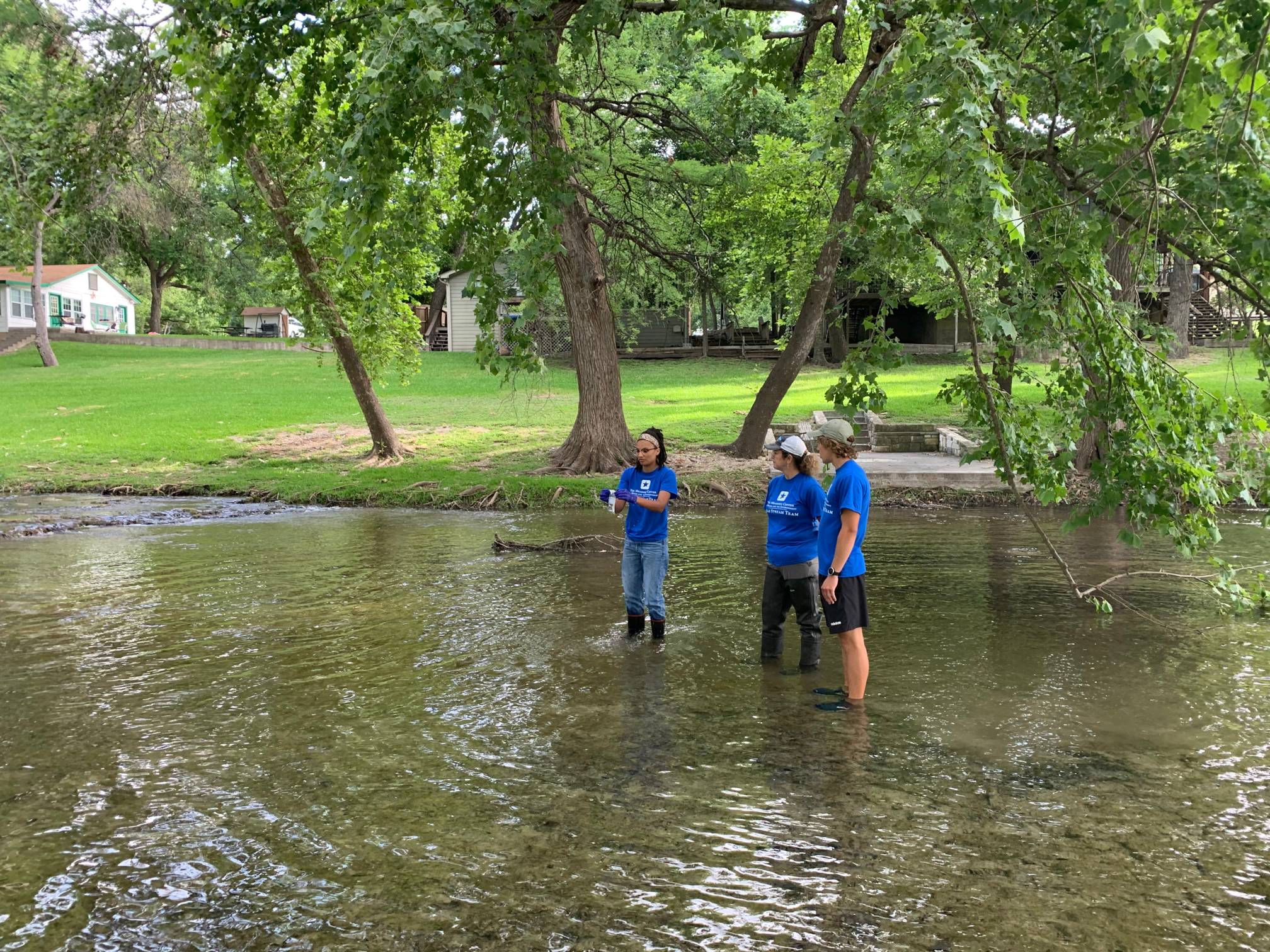 three people in blue shirts standing in shin-deep water