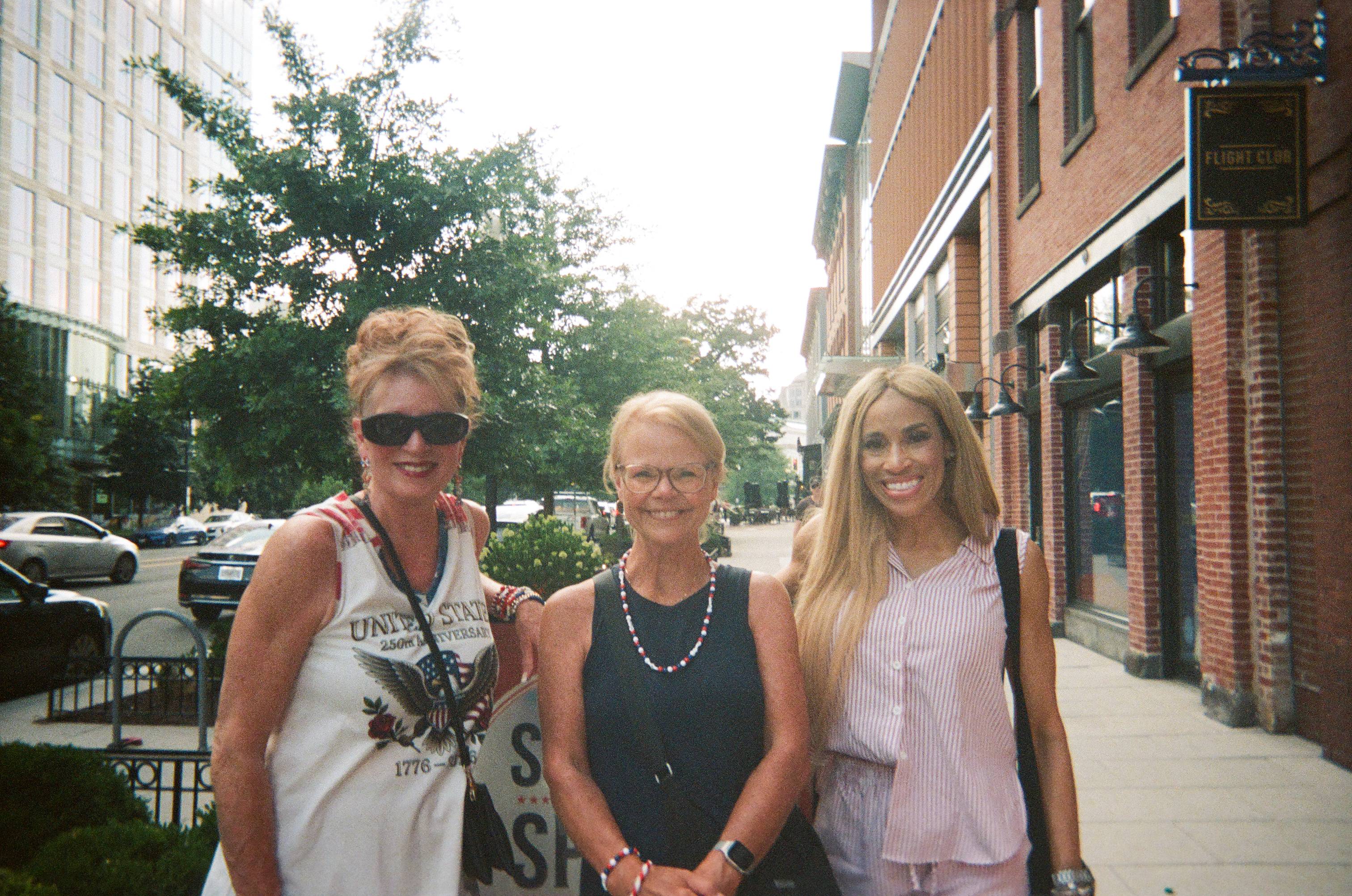 three women pose for photo on sidewalk