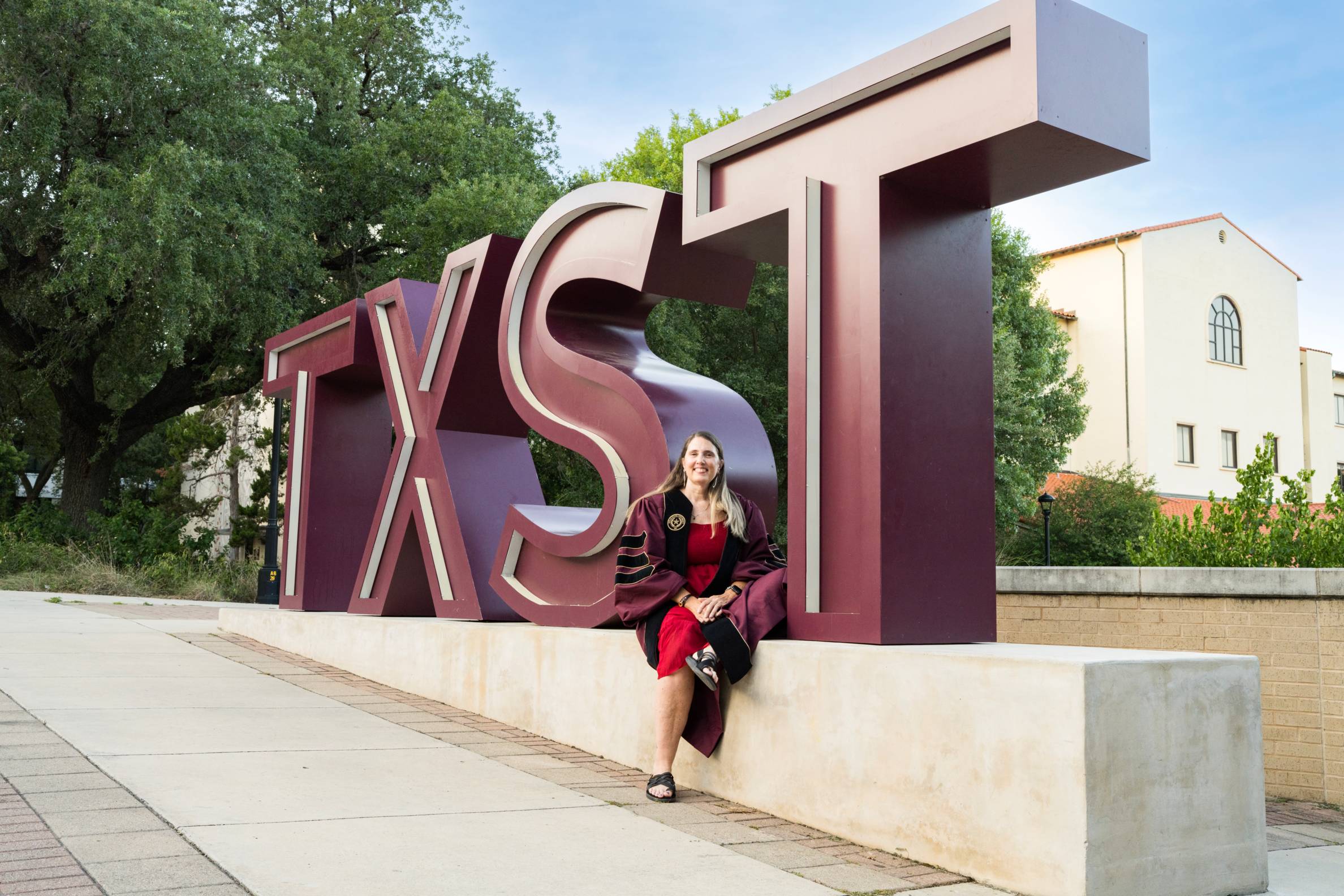 beth sits in front of the txst letters sign in graduation gown