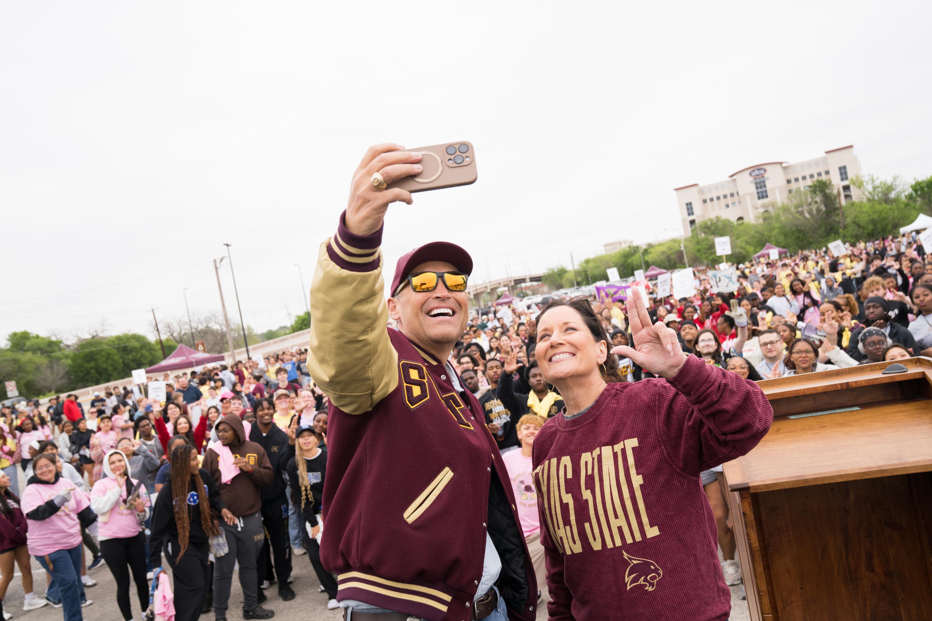 President Damphousse and Beth Damphousse take selfie in front of large crowd of students
