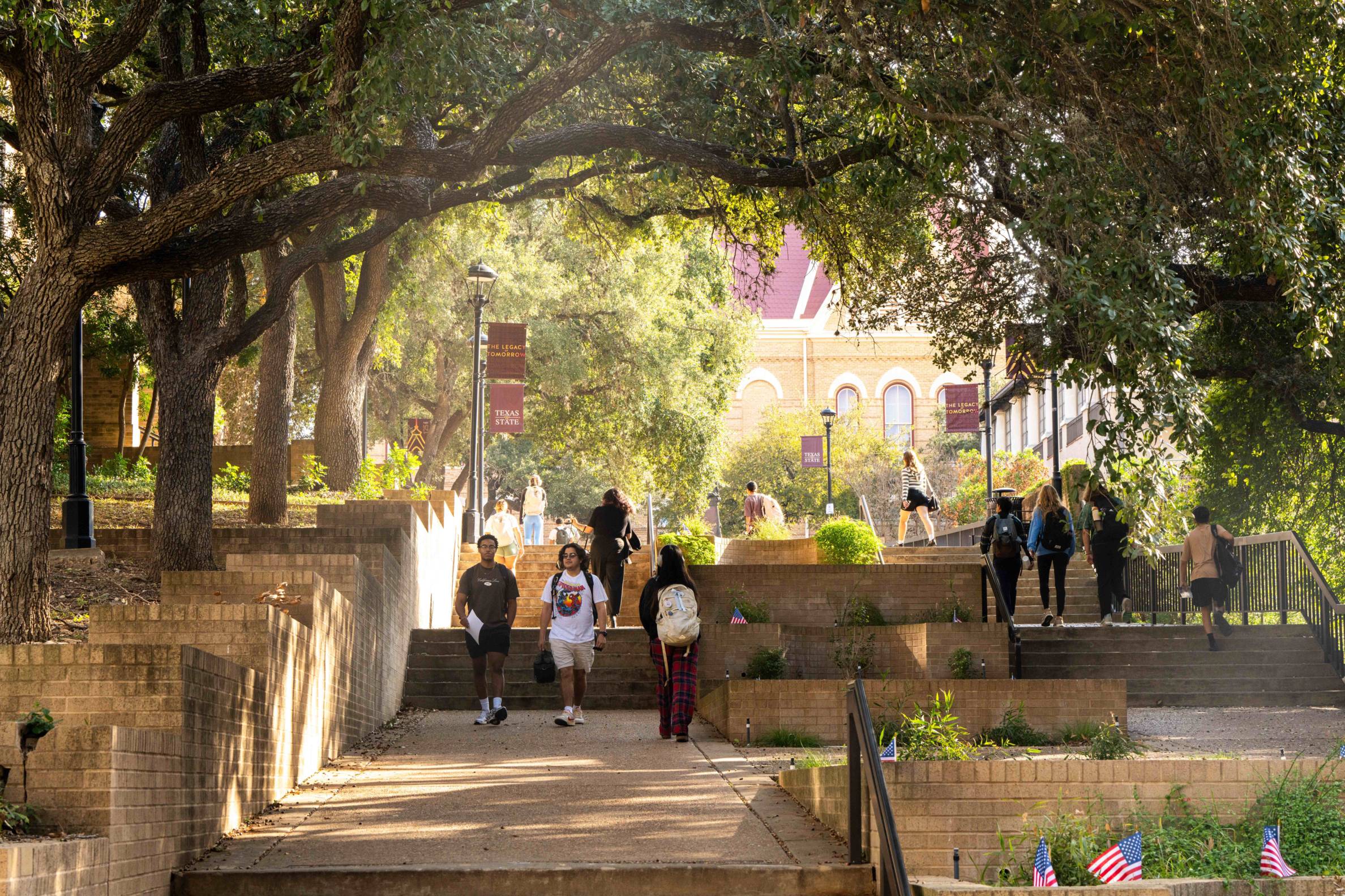students walk in a shady area of txst san marcos campus