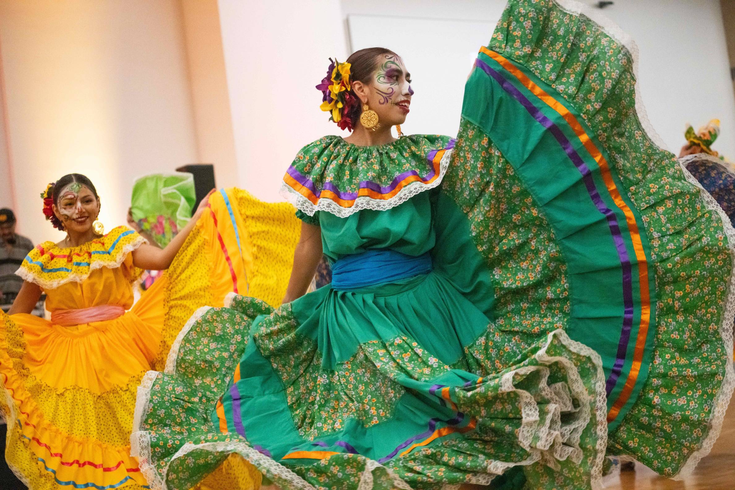 girl wears colorful teal dress and dances with flowers in her hair and face painted with dia de lost muertos makeup