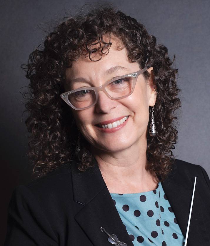 Elizabeth Chappell headshot, curly brunette with vintage glasses holding a conductor's baton