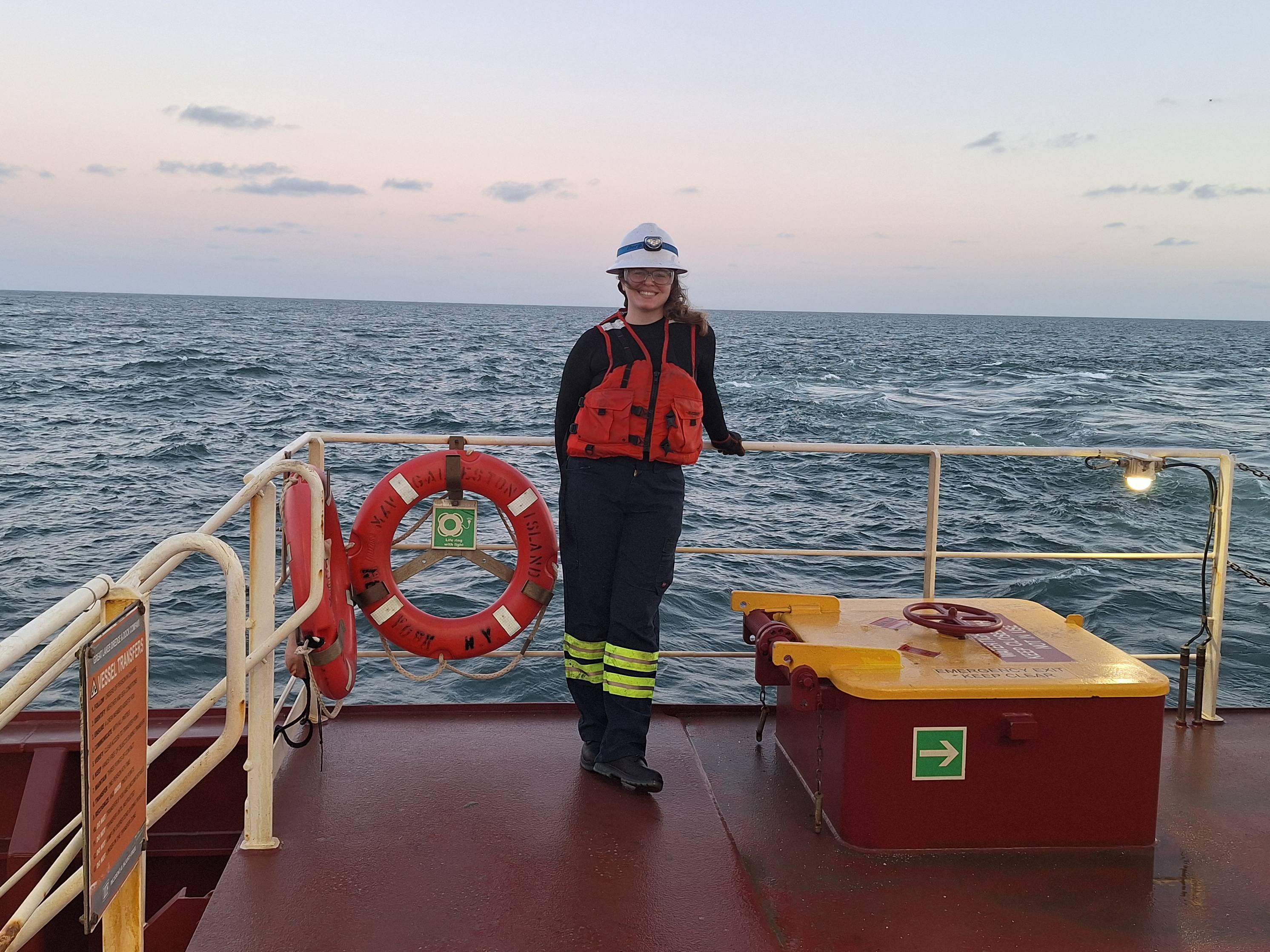woman in hard hat and life vest standing on off-shore rig with ocean behind her