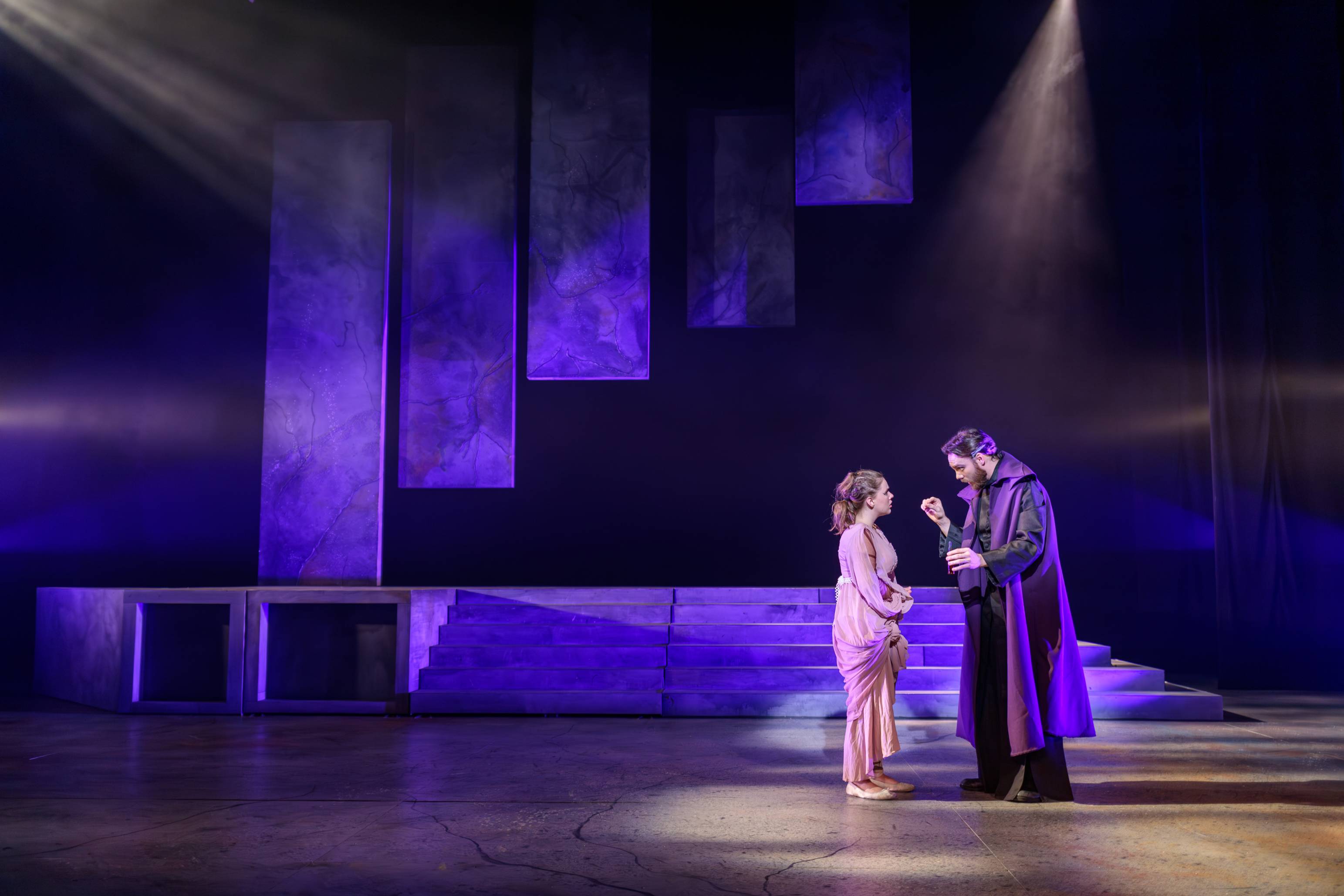 two actors performing on stage with dramatic purple lighting