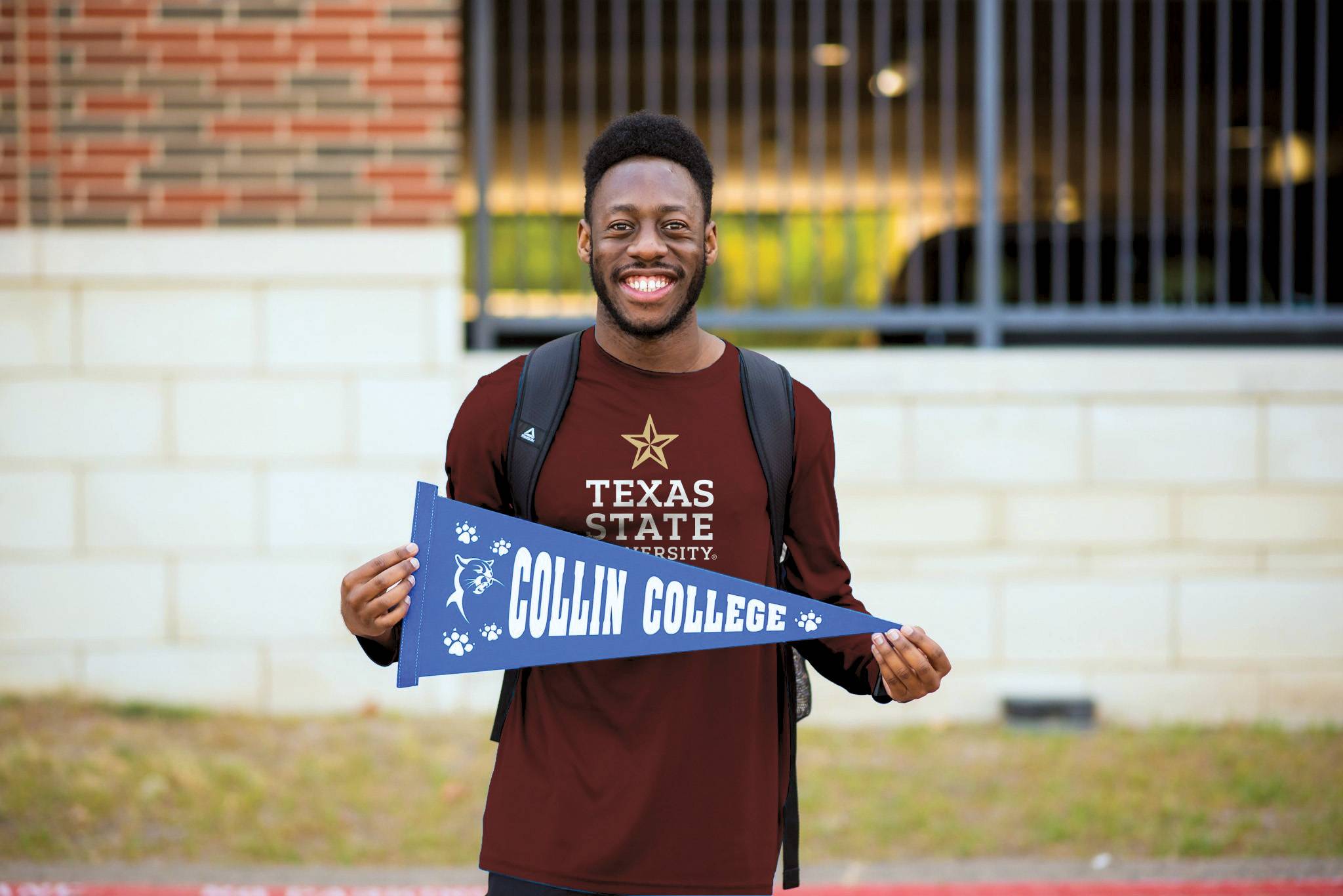 young man wears a maroon txst t-shirt and holds a blue collin college banner