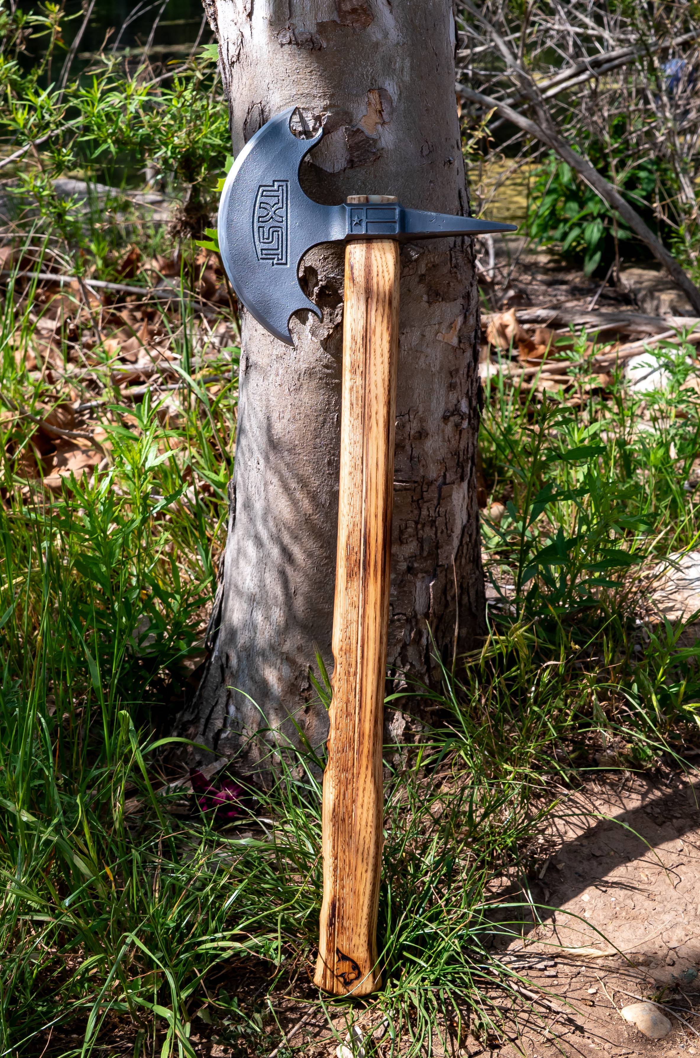 forged steel axe with wooden handle leaning against a tree