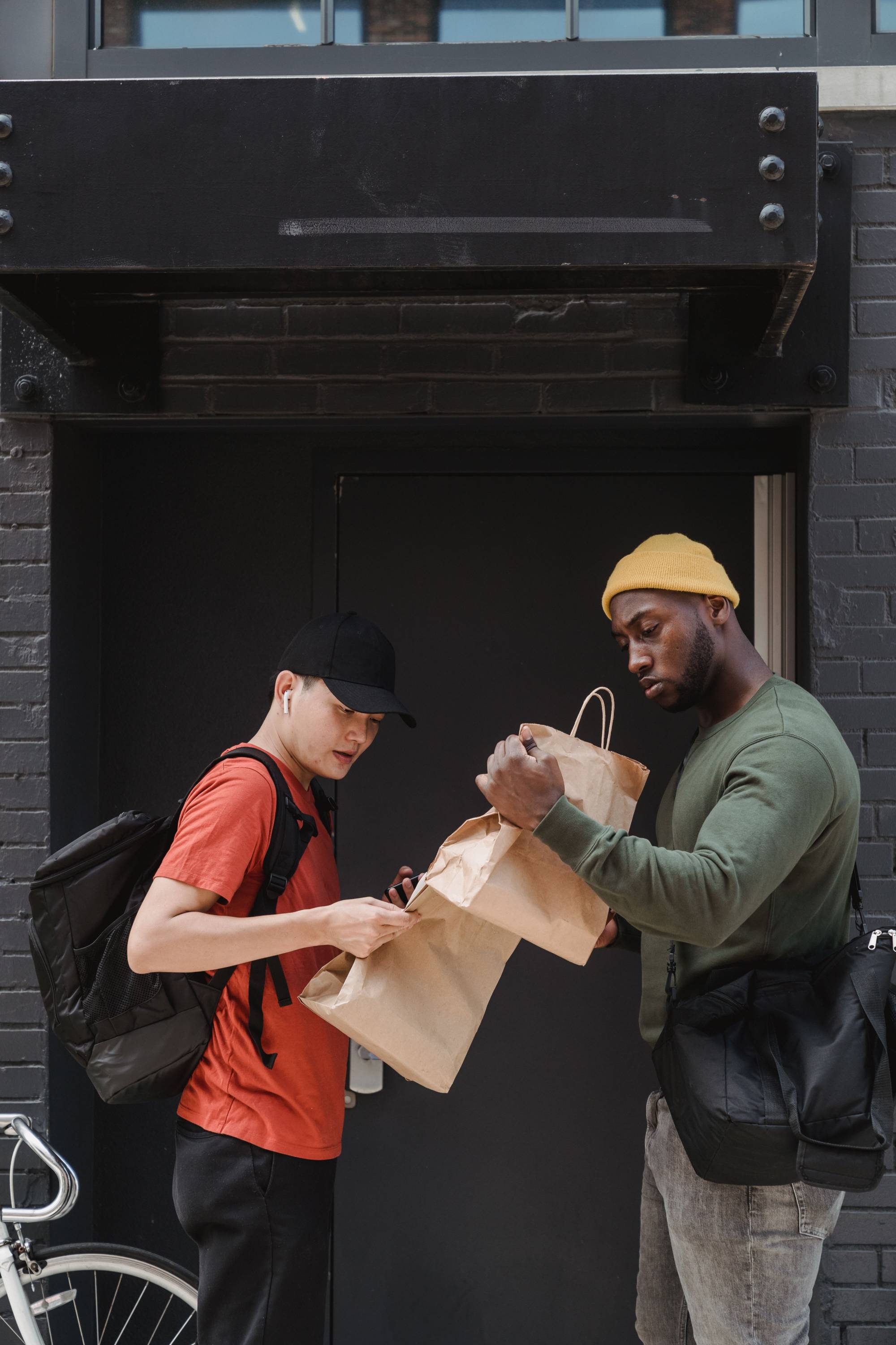 Gig economy worker hands a takeout order to a delivery driver outside a business. The image represents app-based work, independent contracting, delivery services, self-employment, and tax responsibilities for gig workers, including income reporting, deductions, and estimated taxes.