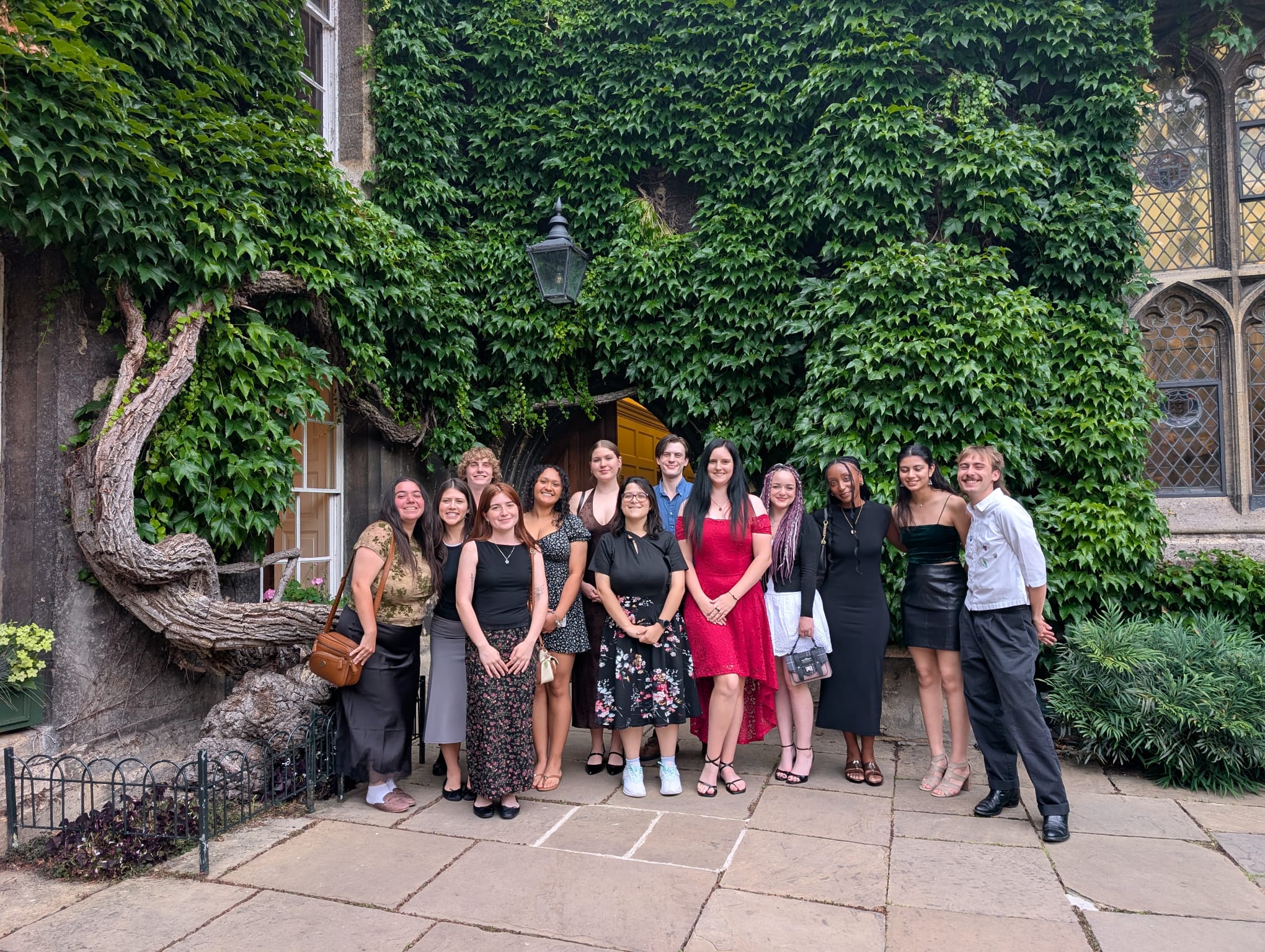 group of students standing together smiling for a picture in front of ivy covered wall.