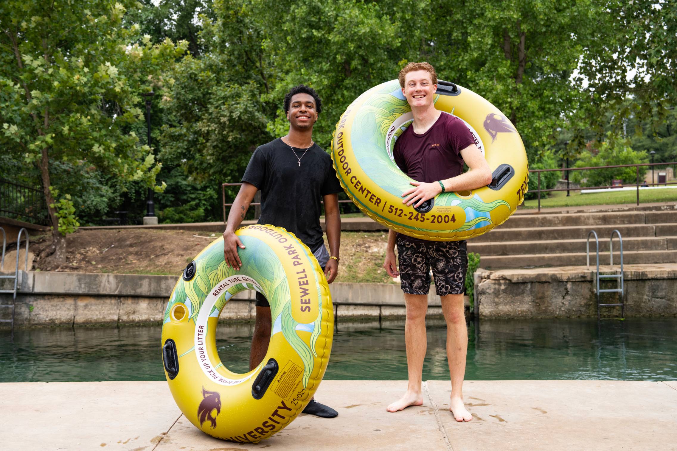 two male students holding tubes by the river