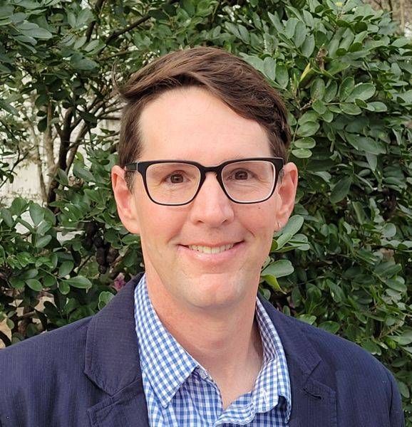 headshot of man standing in front of greenery 