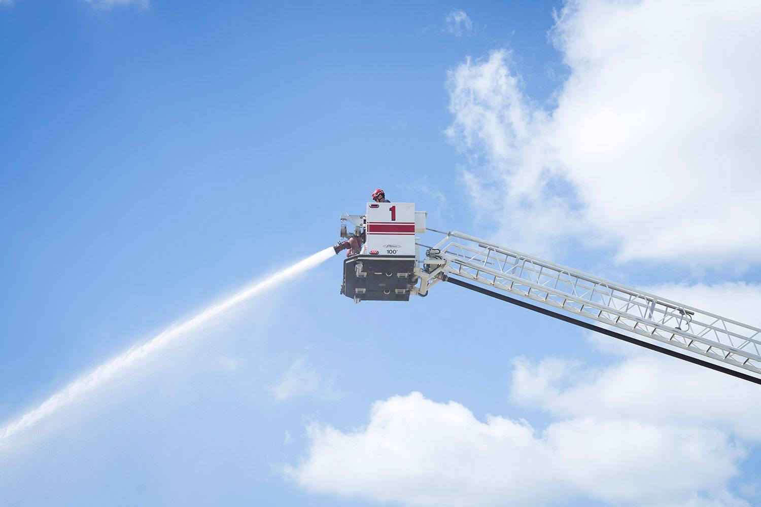 A firefighter at the top of a ladder sprays a firehose.