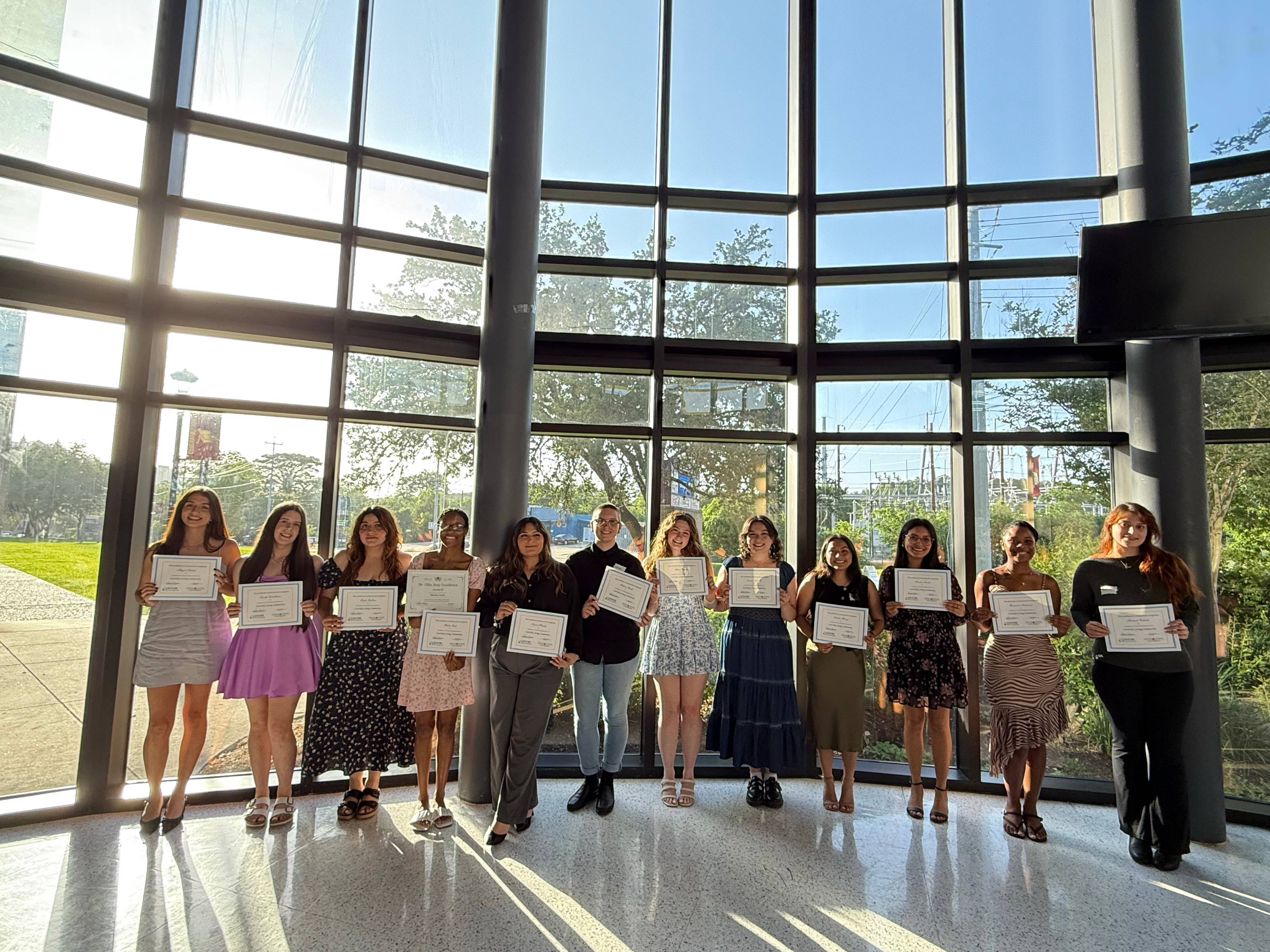 12 people standing in a row while holding up paper certificates