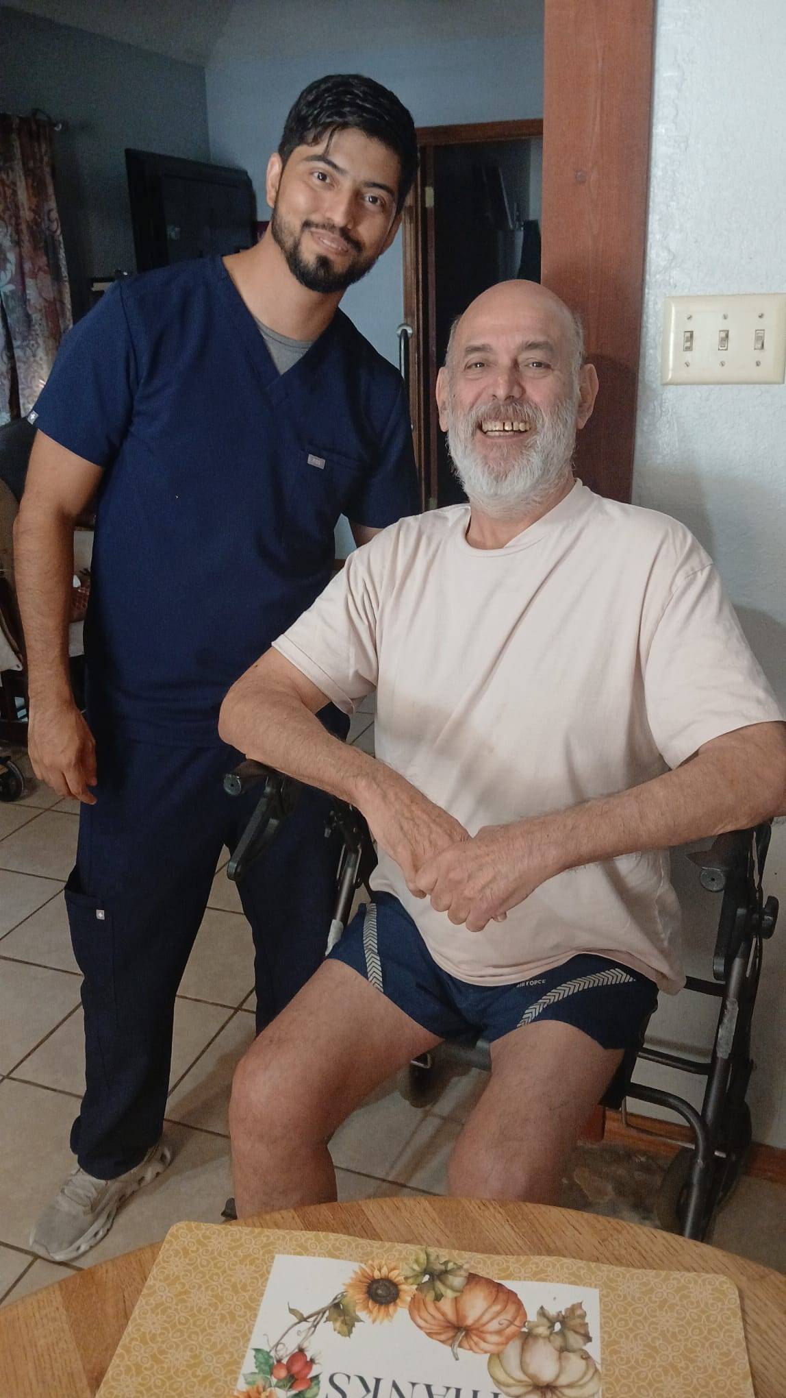 man in navy medical scrubs stands next to older man in wheelchair. they are both smiling for a photo