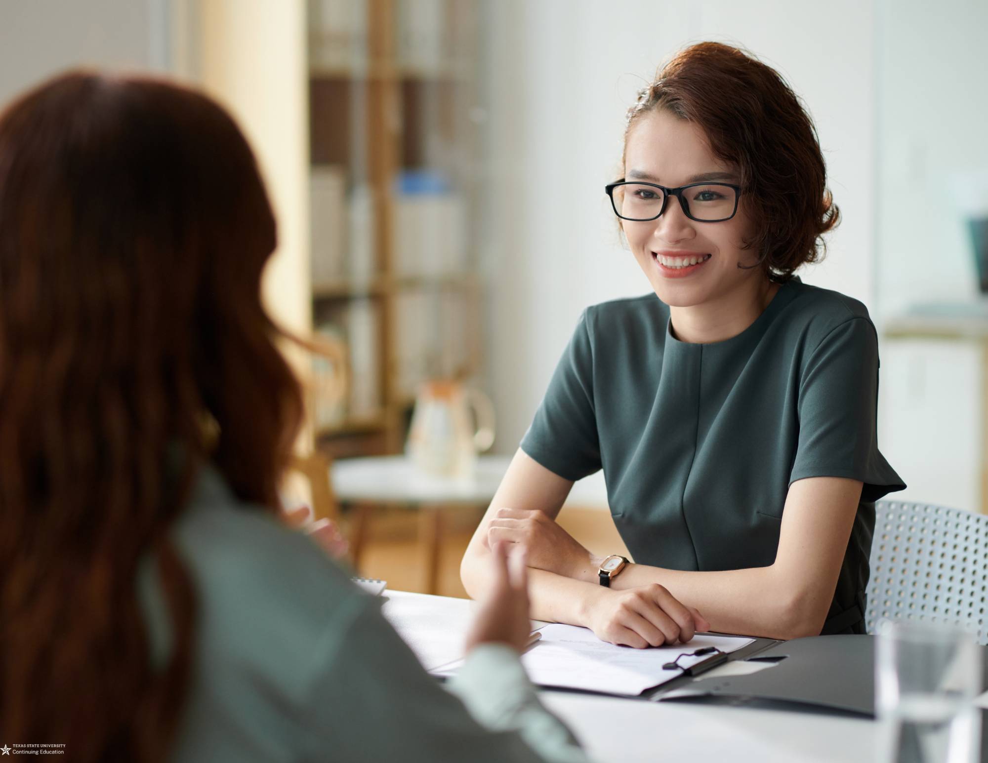 a woman at a desk talking to another woman