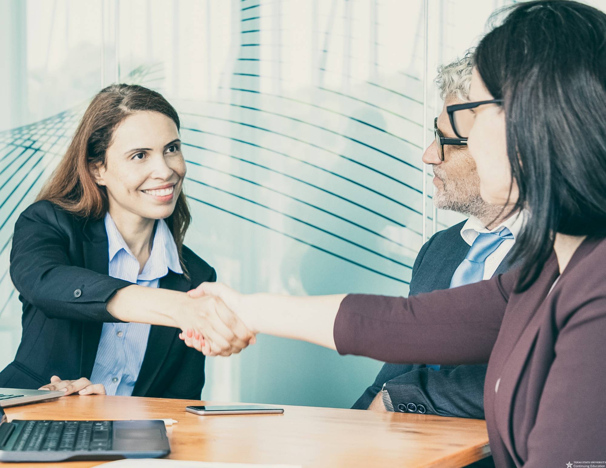 two women shaking hands with a man smiling in the background