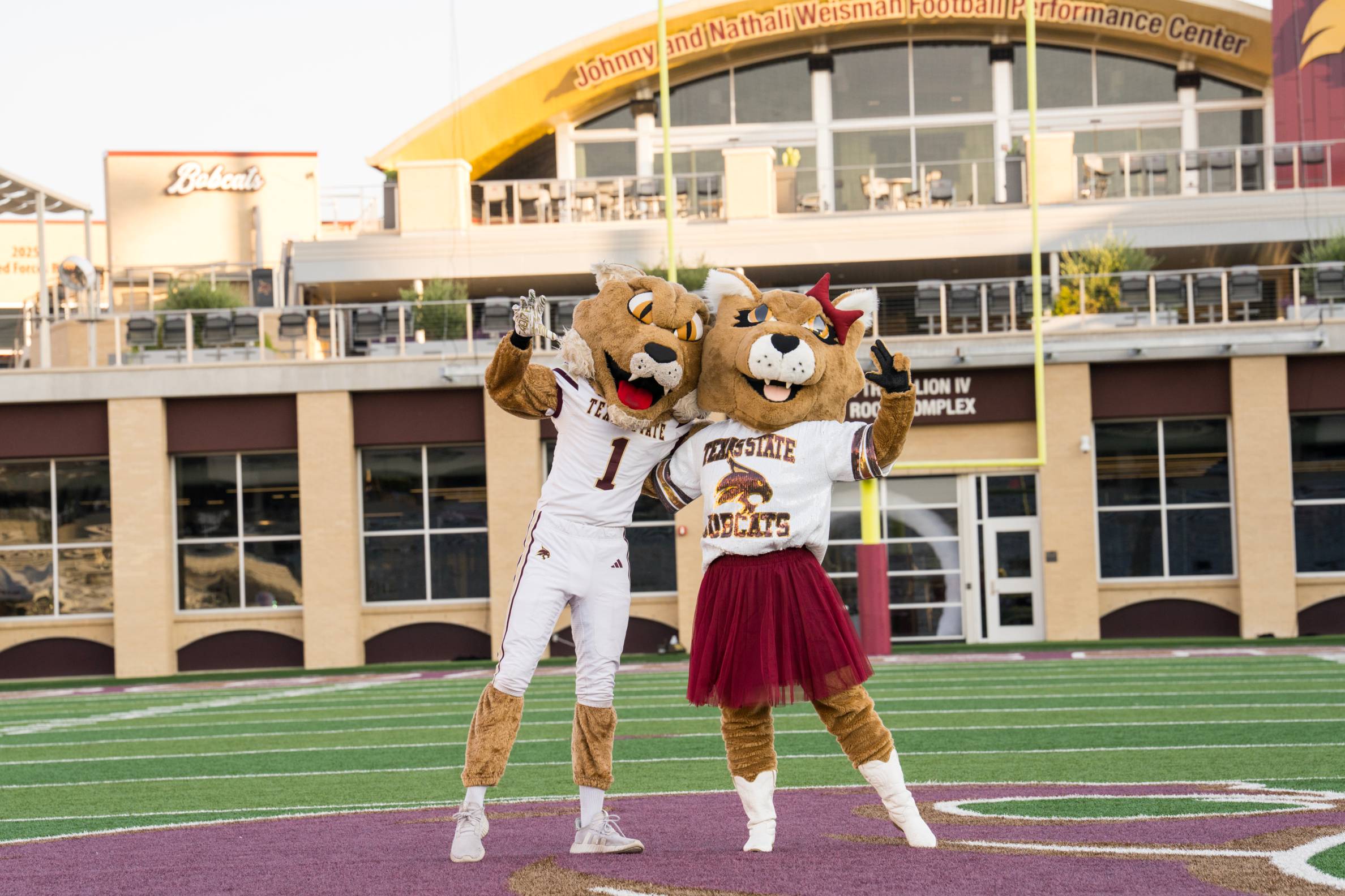 male and female bobcat mascots pose on football field
