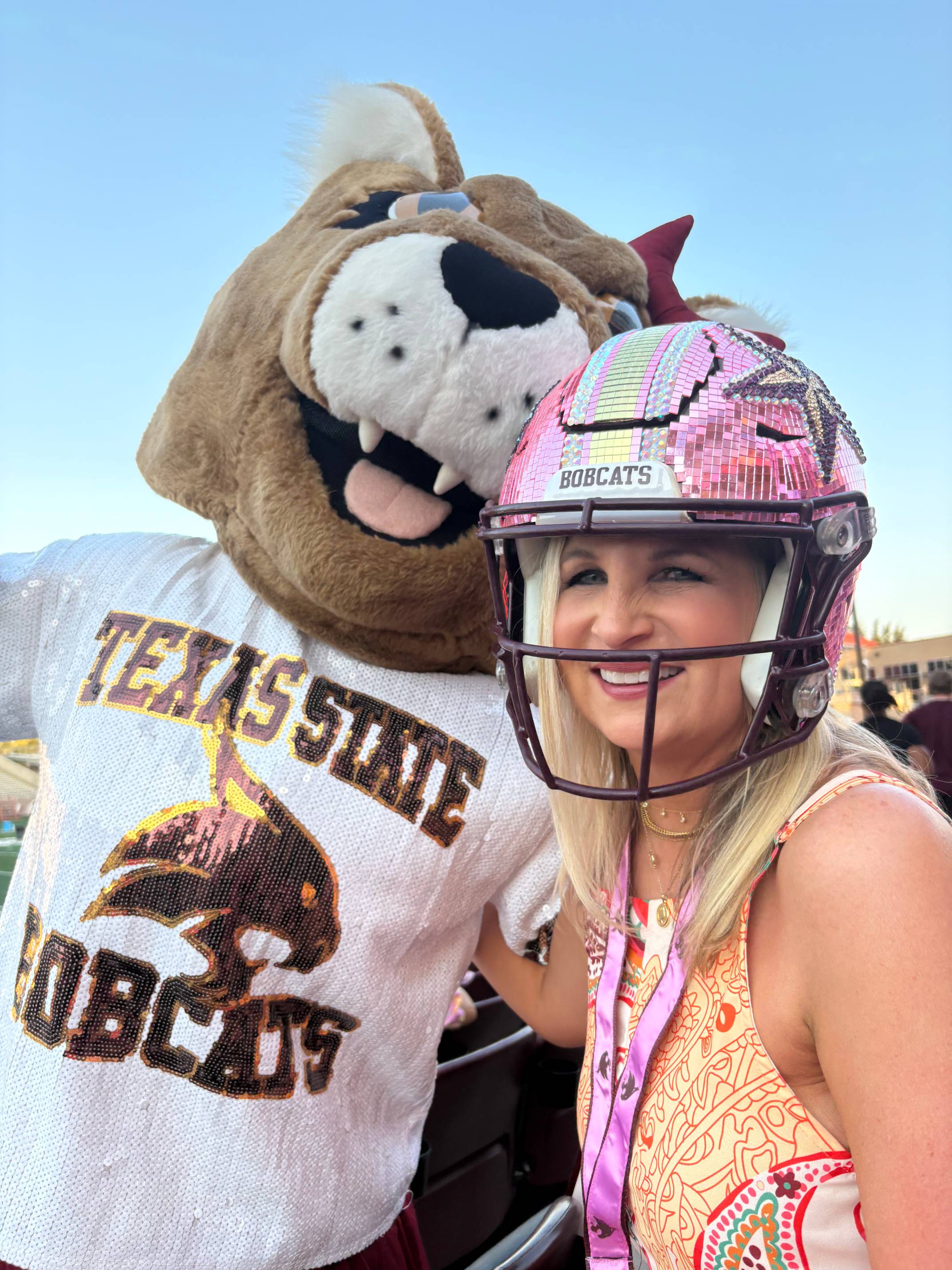 woman in pink sparkly football helmet takes photo with female bobcat mascot