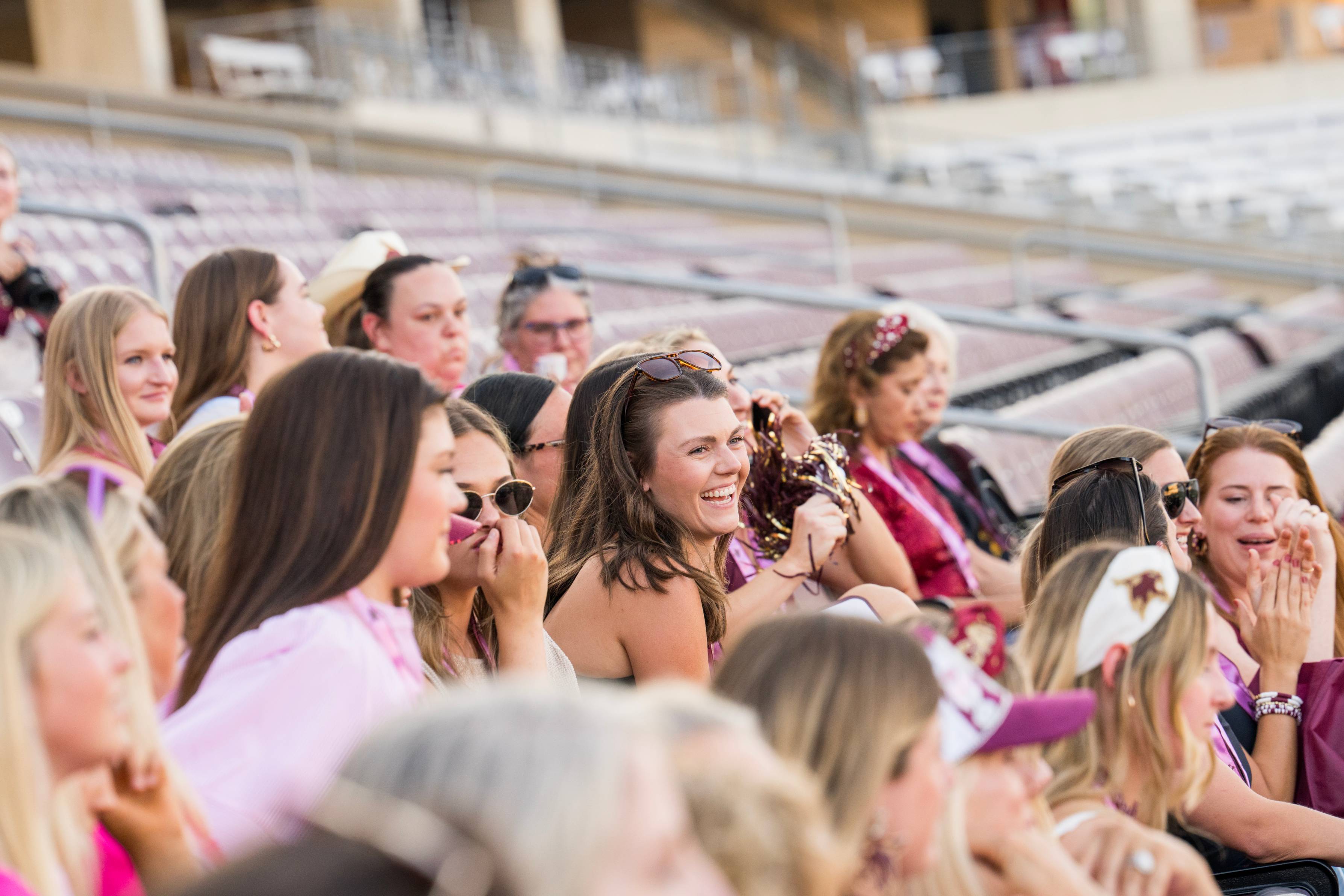 women laugh and smile as they sit in football stadium seats
