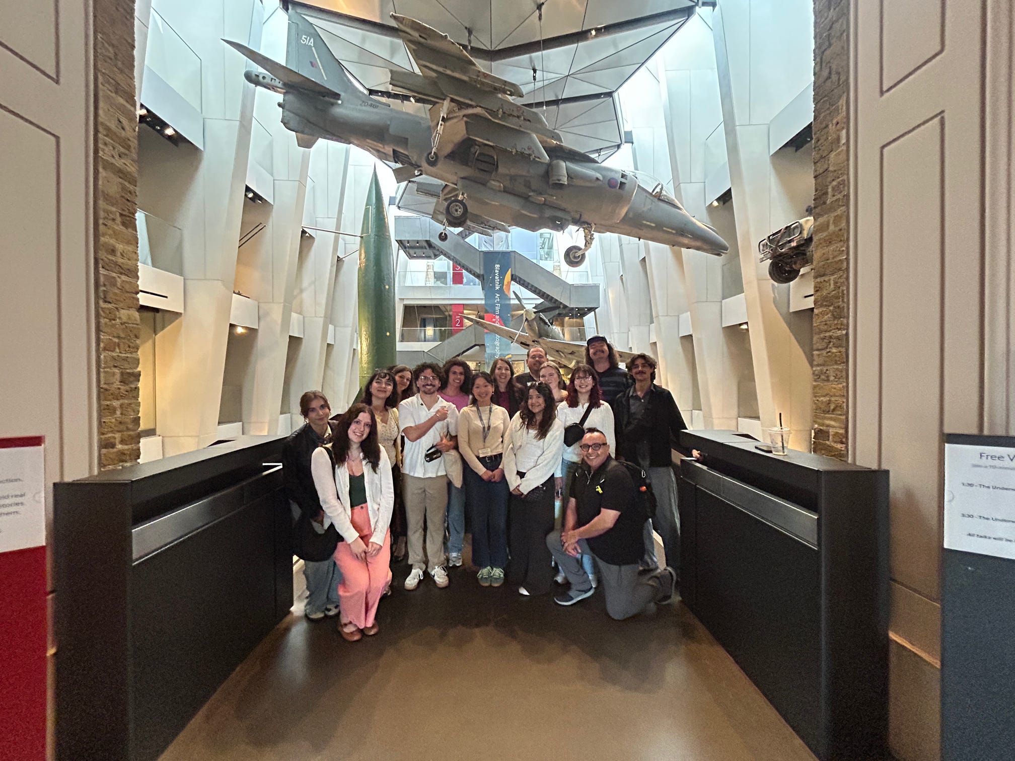 A group of Texas State students and staff members standing under a fighter jet installation at the Imperial War Museum in London