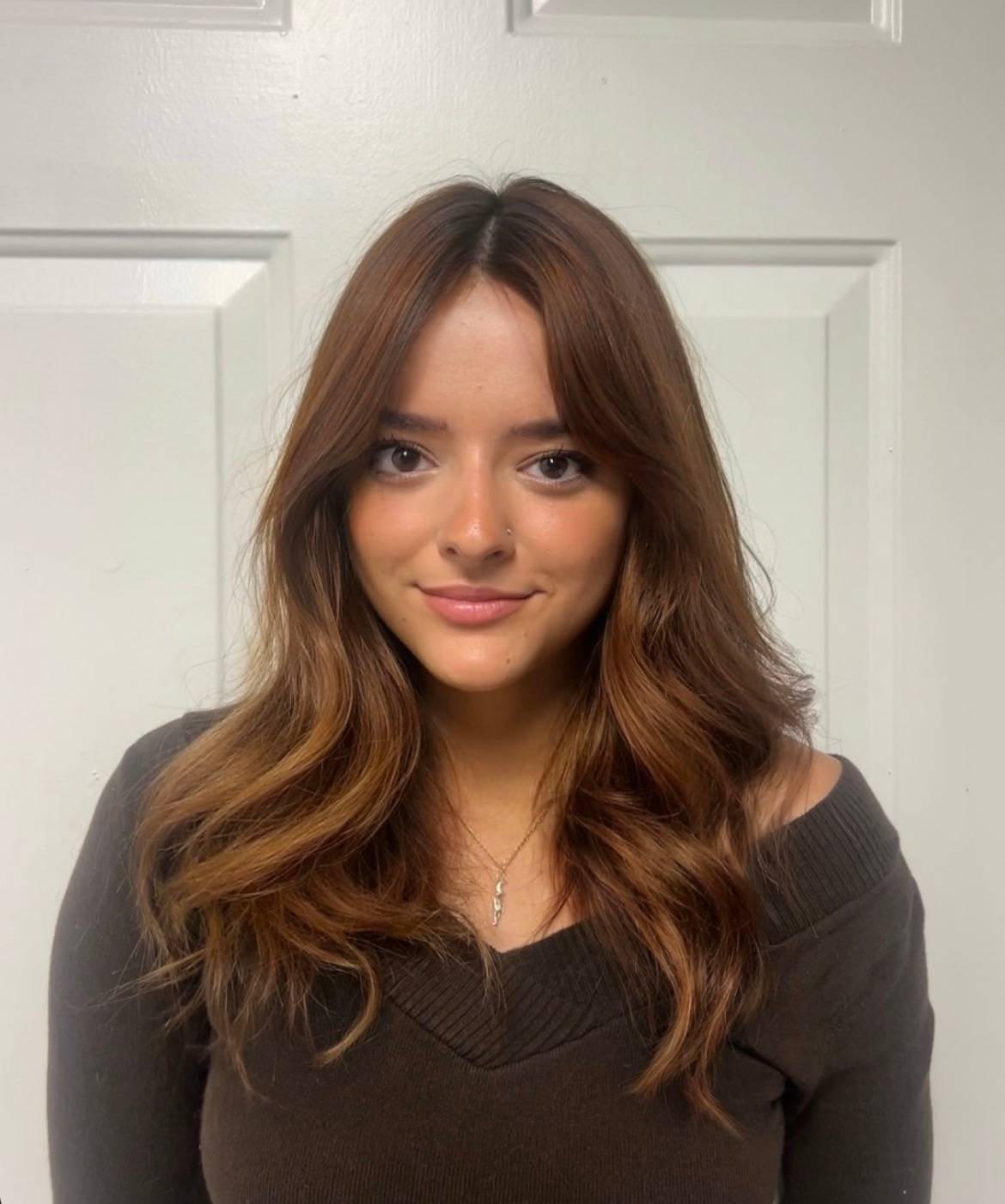 woman with long brown hair, brown sweater, standing in front of door