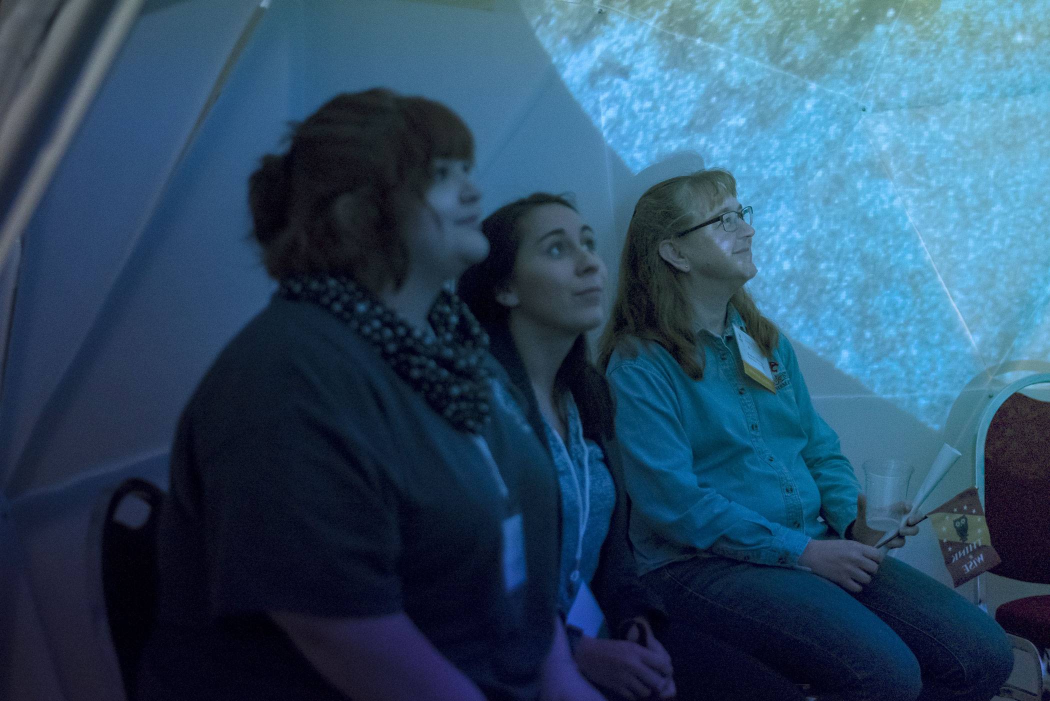 Group of students watch constellations projected inside a geodesic dome.