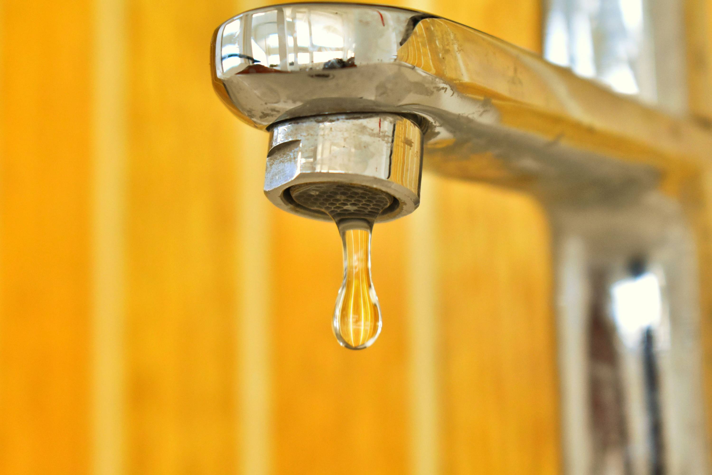 A close up of a leaking faucet with bright yellow wooden background