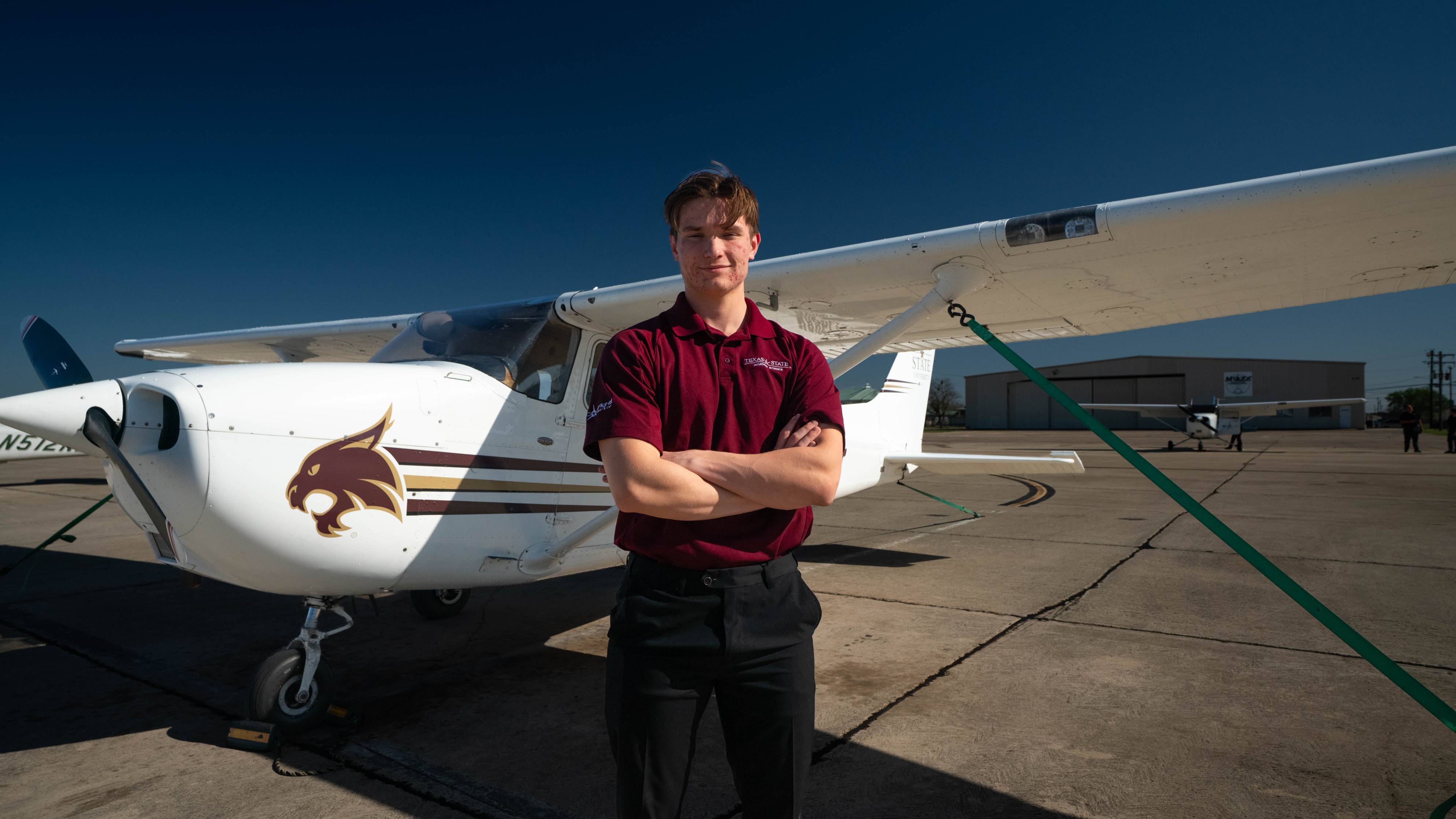 A student stands in front of TXST propeller plane