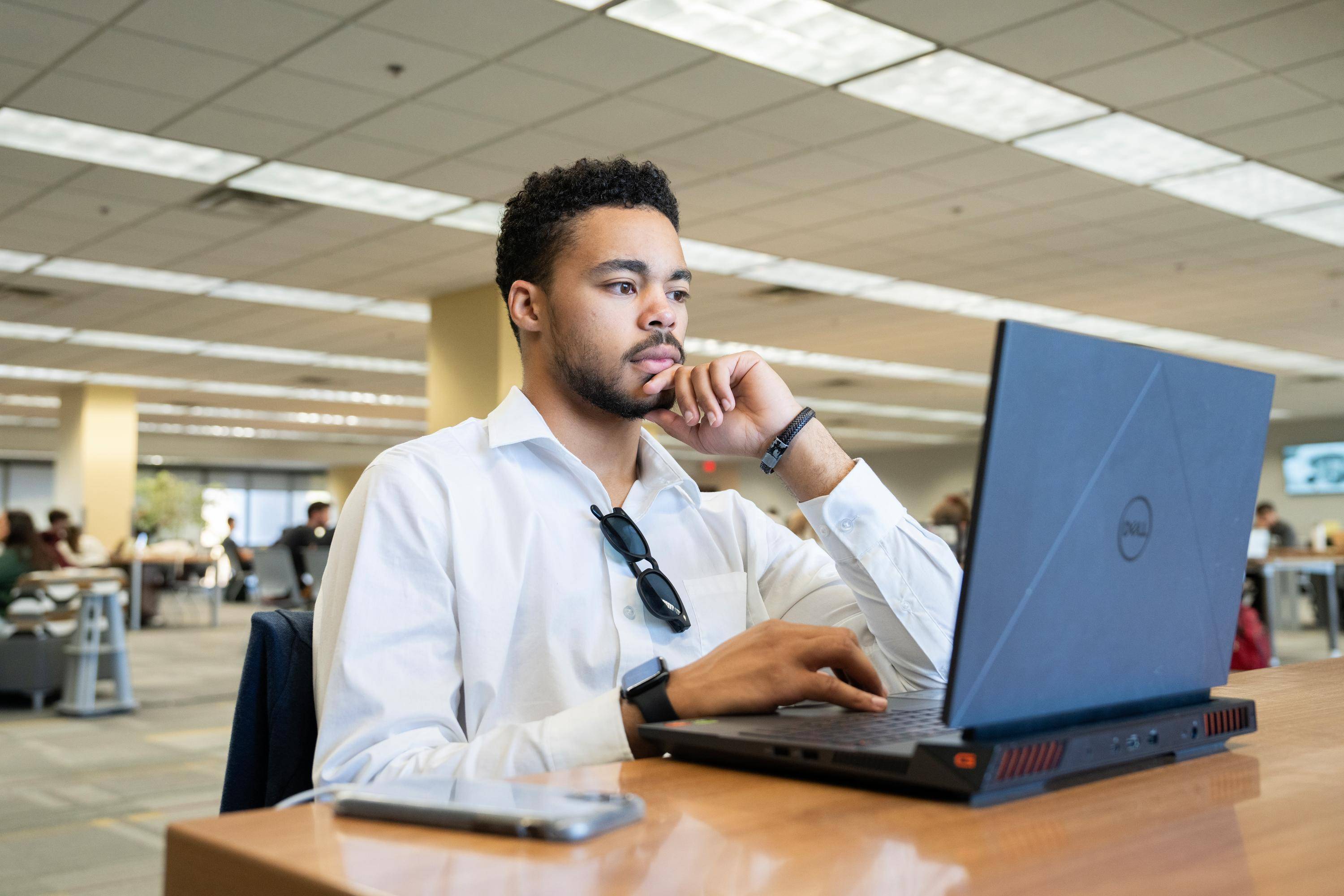 man in white button down shirt looking at laptop while sitting in library setting