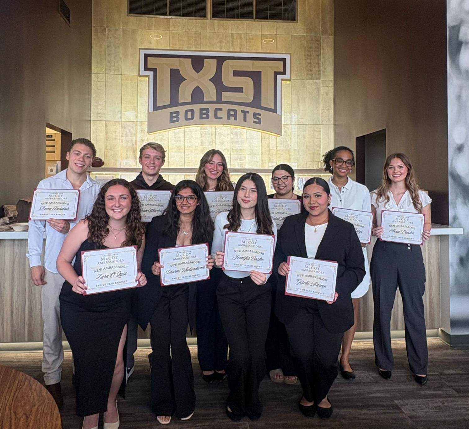 Ten newly initiated McCoy Ambassadors standing in front of a TXST sign