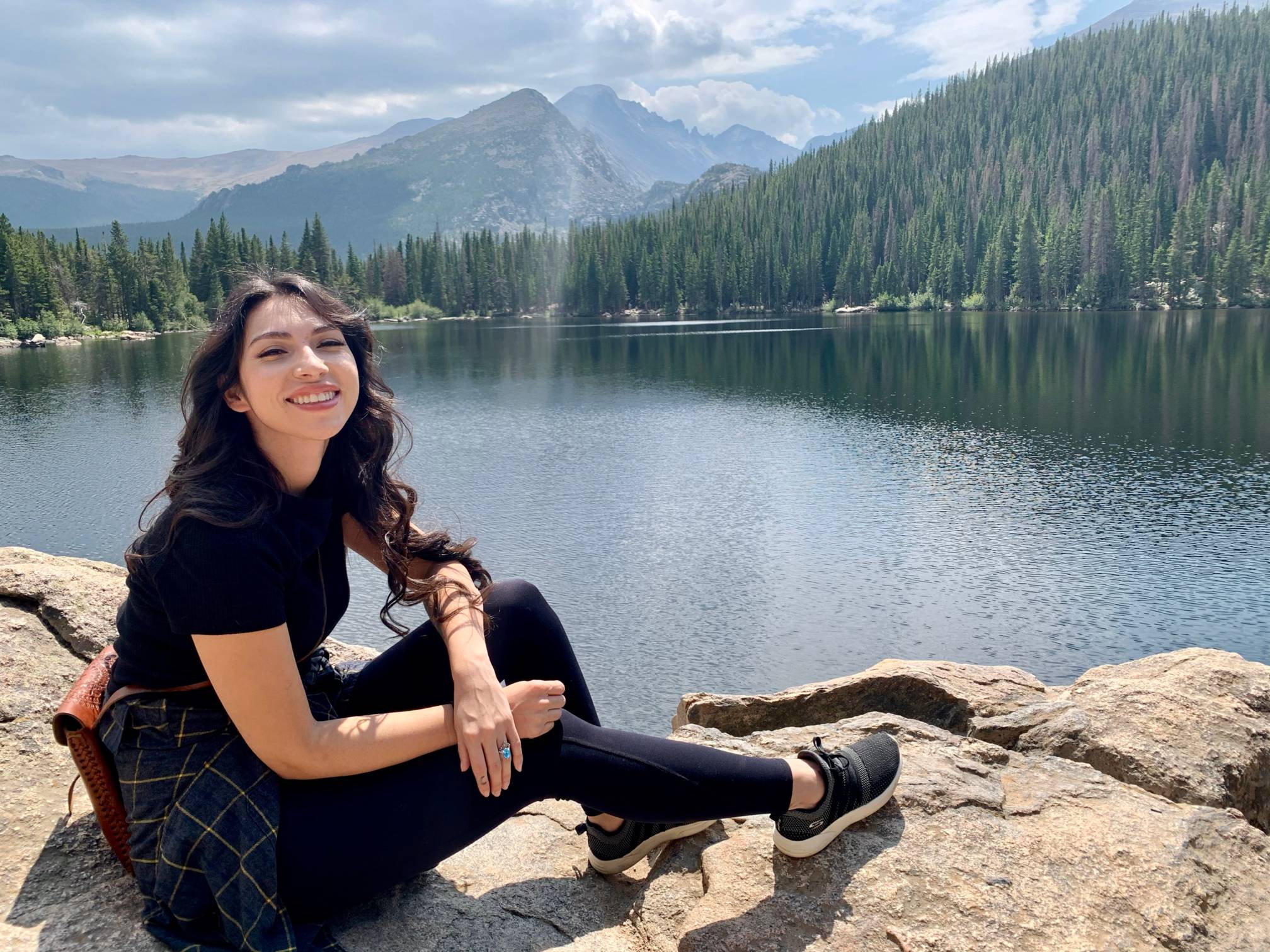 photo of Kelsey hiking, sitting on ledge with alpine lake and mountains behind her