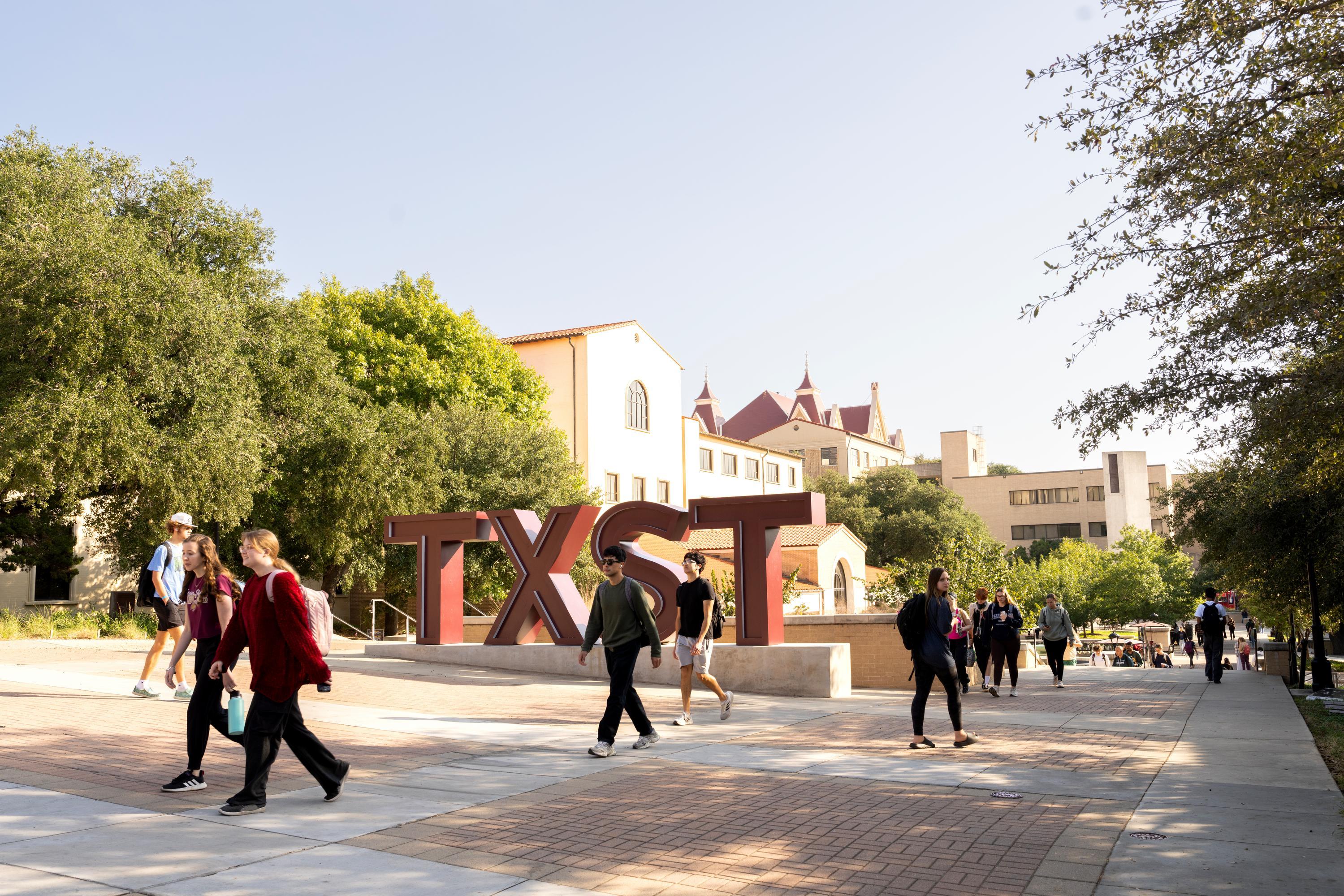 students walking on campus next to large TXST sign