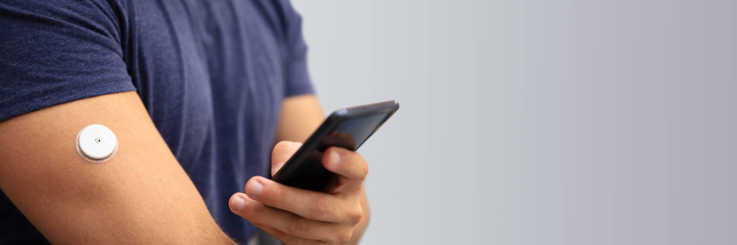 A person holding a cellphone while wearing a continuous glucose monitor
