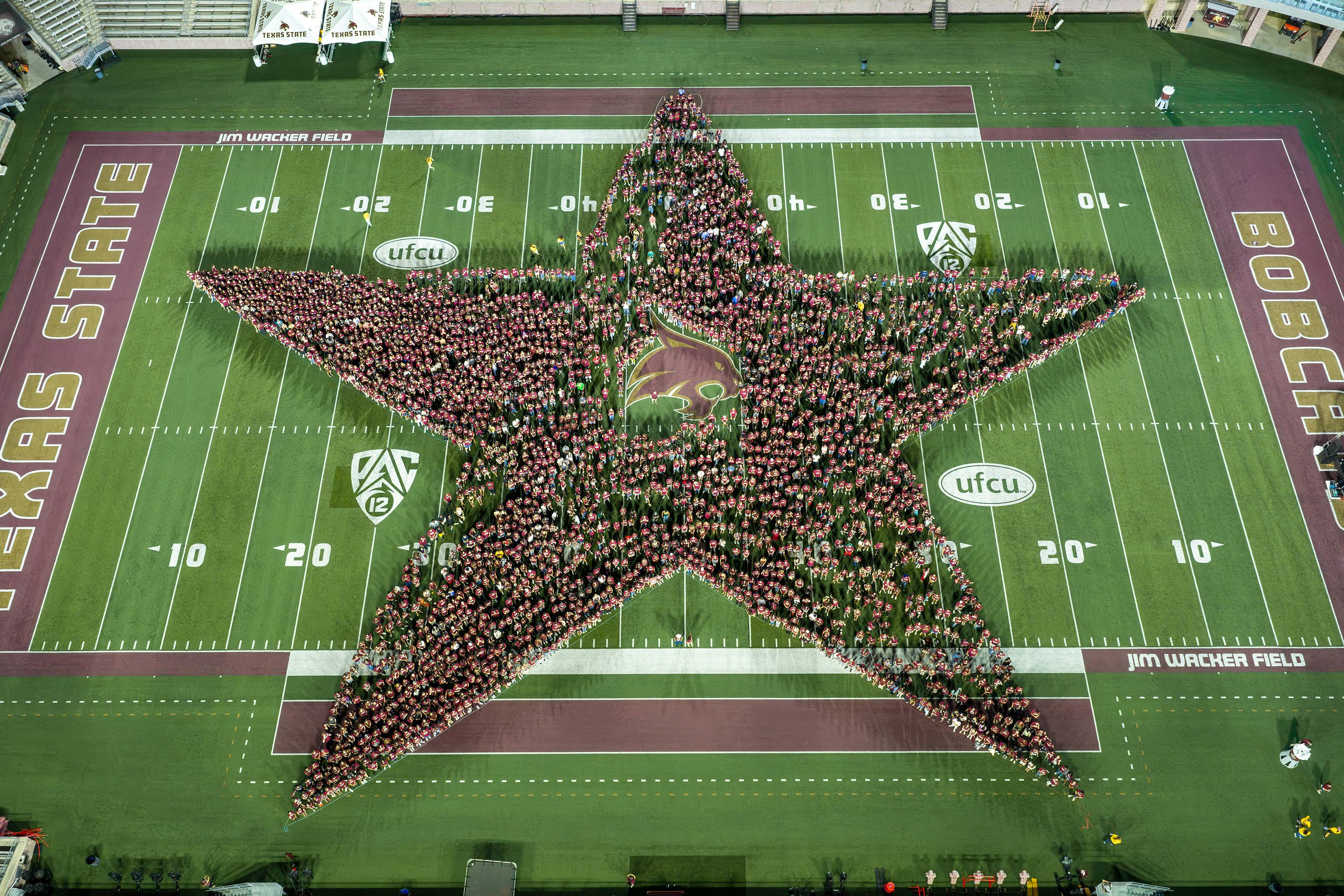 large group of students forming the shape of a star on the txst football field