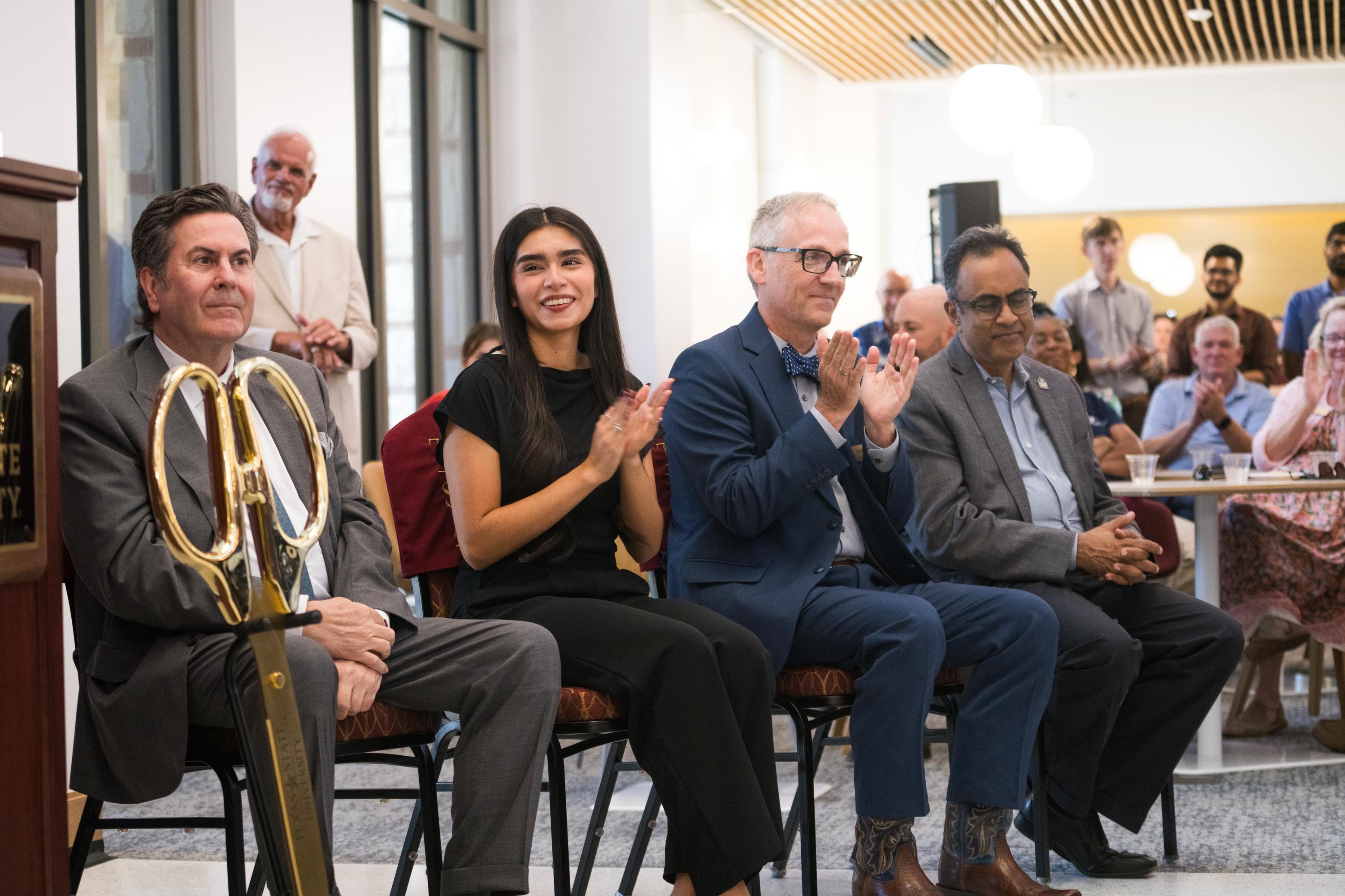 four people clapping while listening to speaker