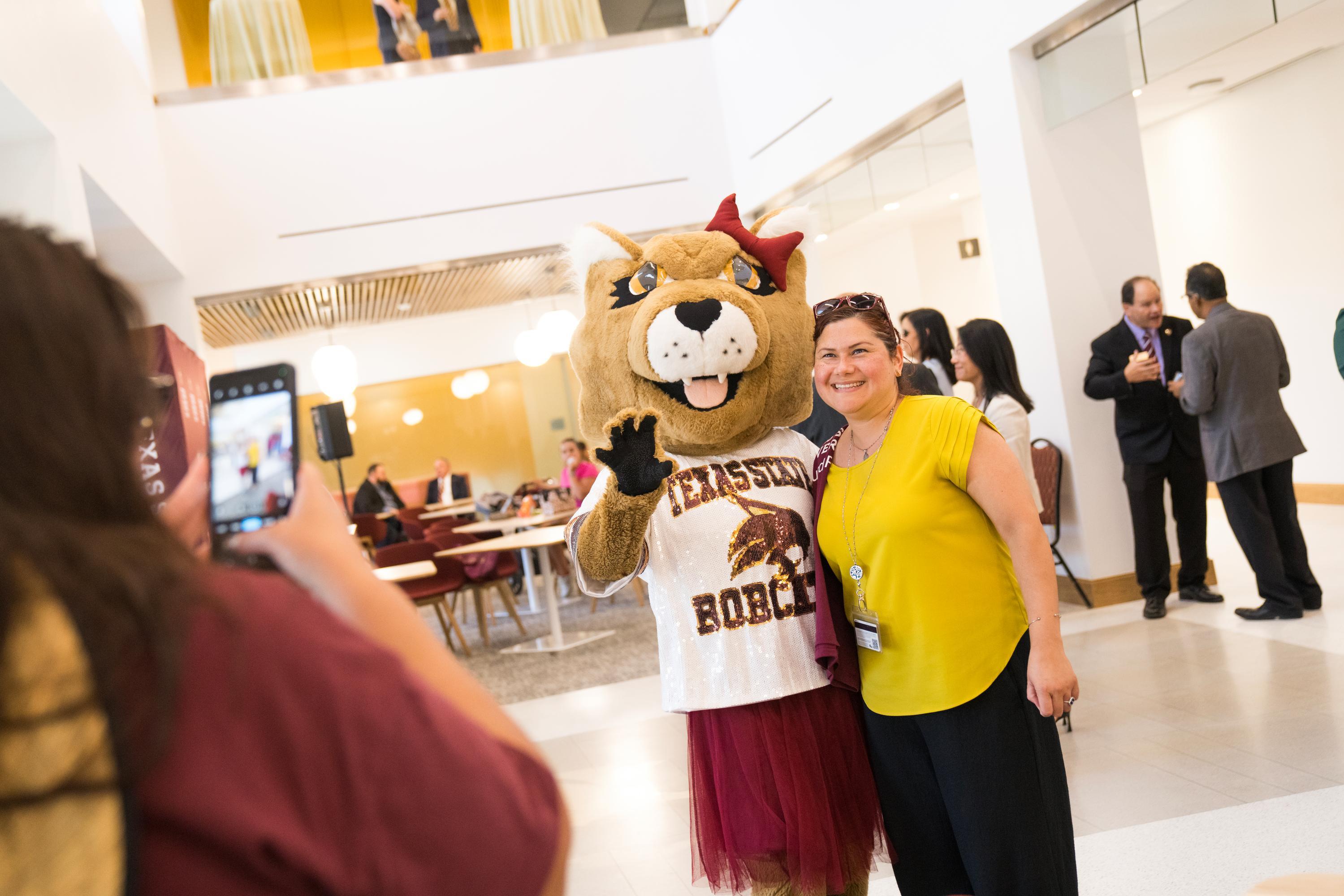 women in yellow shirt poses for photo with female bobcat mascot