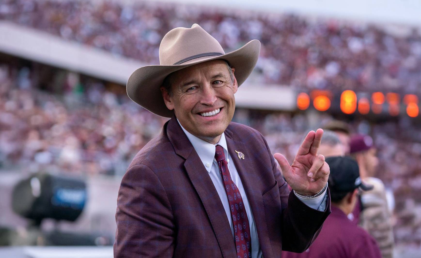 president damphousse smiles during football team while wearing cowboy hat