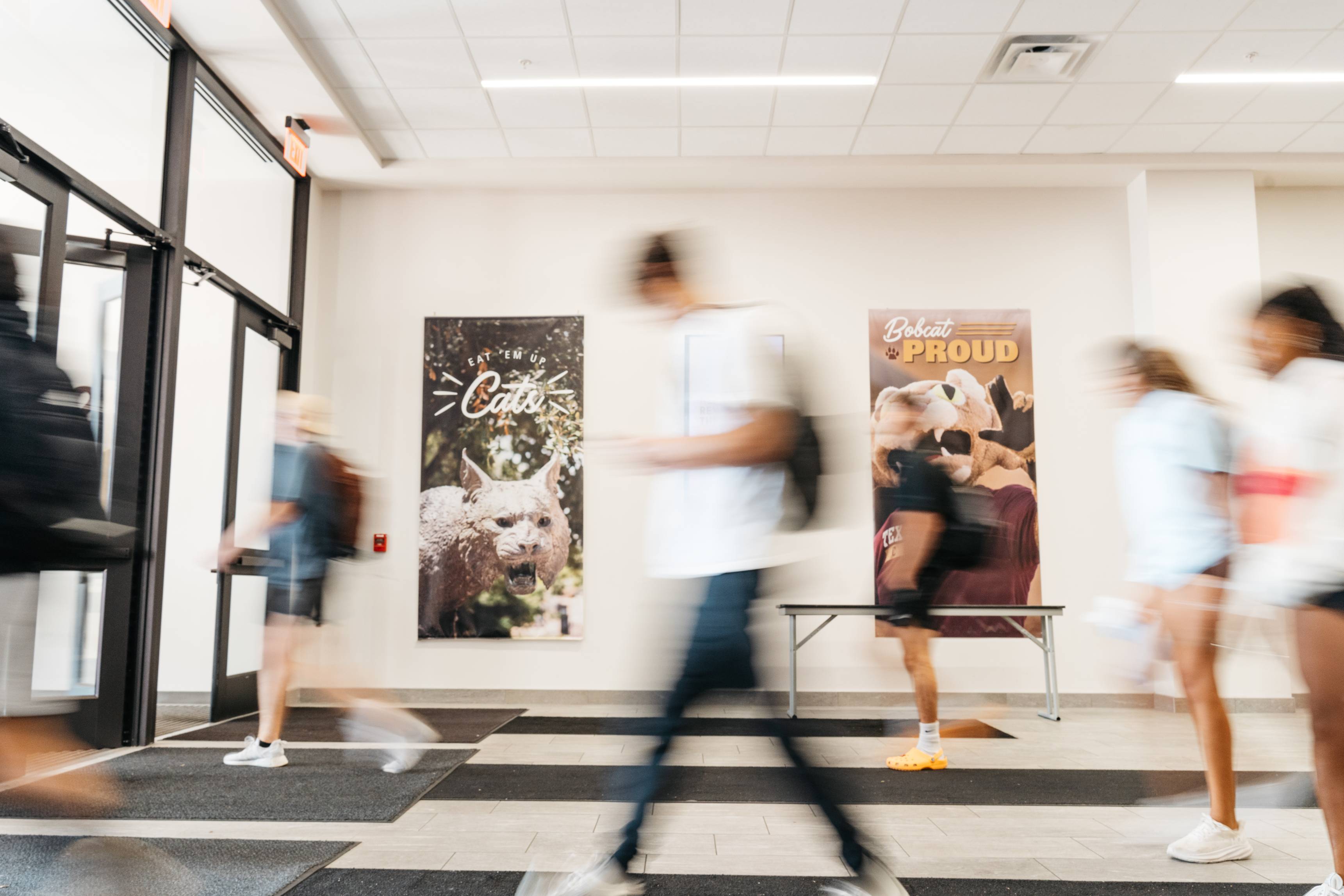 Students walking through a Texas State University building entrance quickly