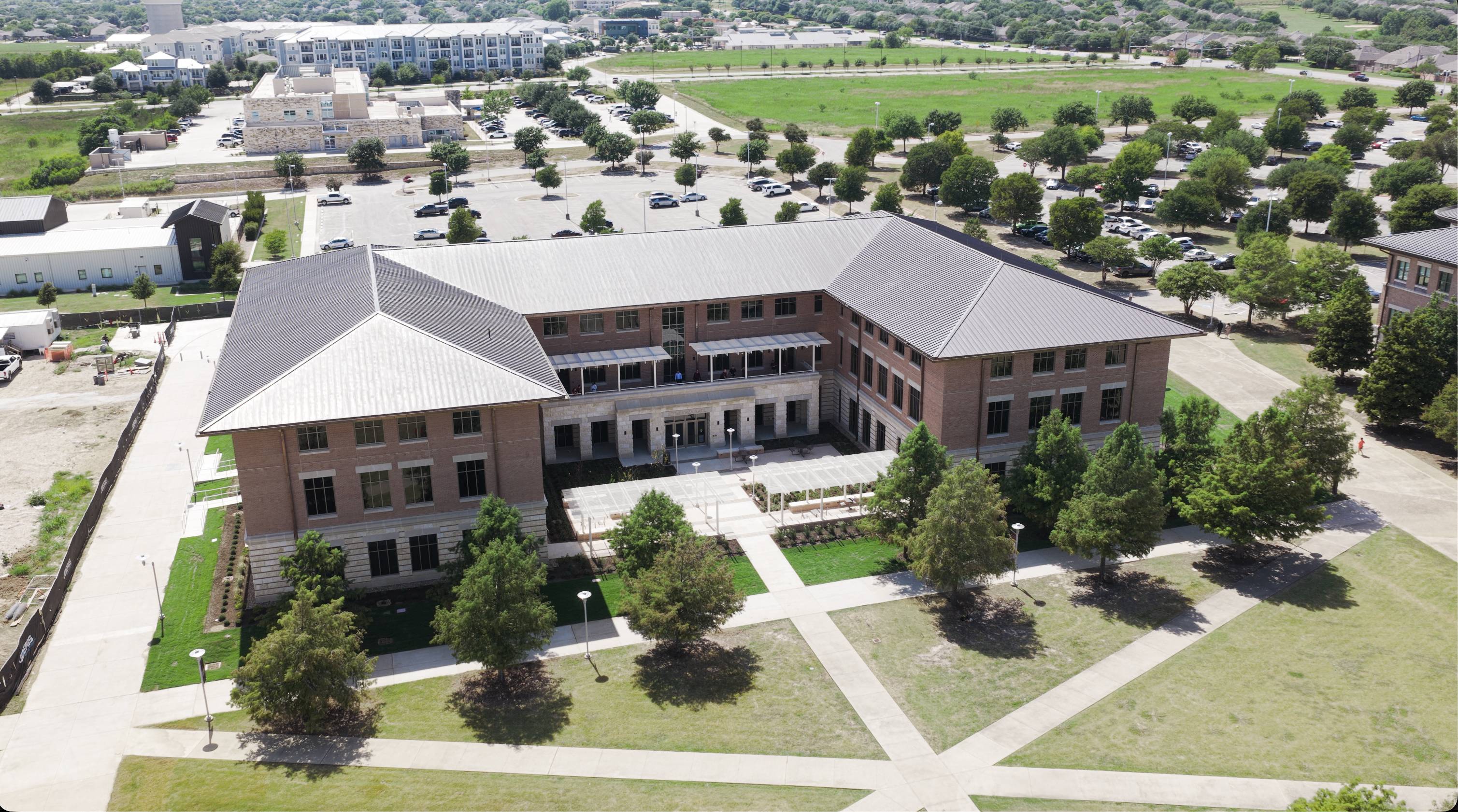 exterior photo of large u-shaped building with line of trees in front