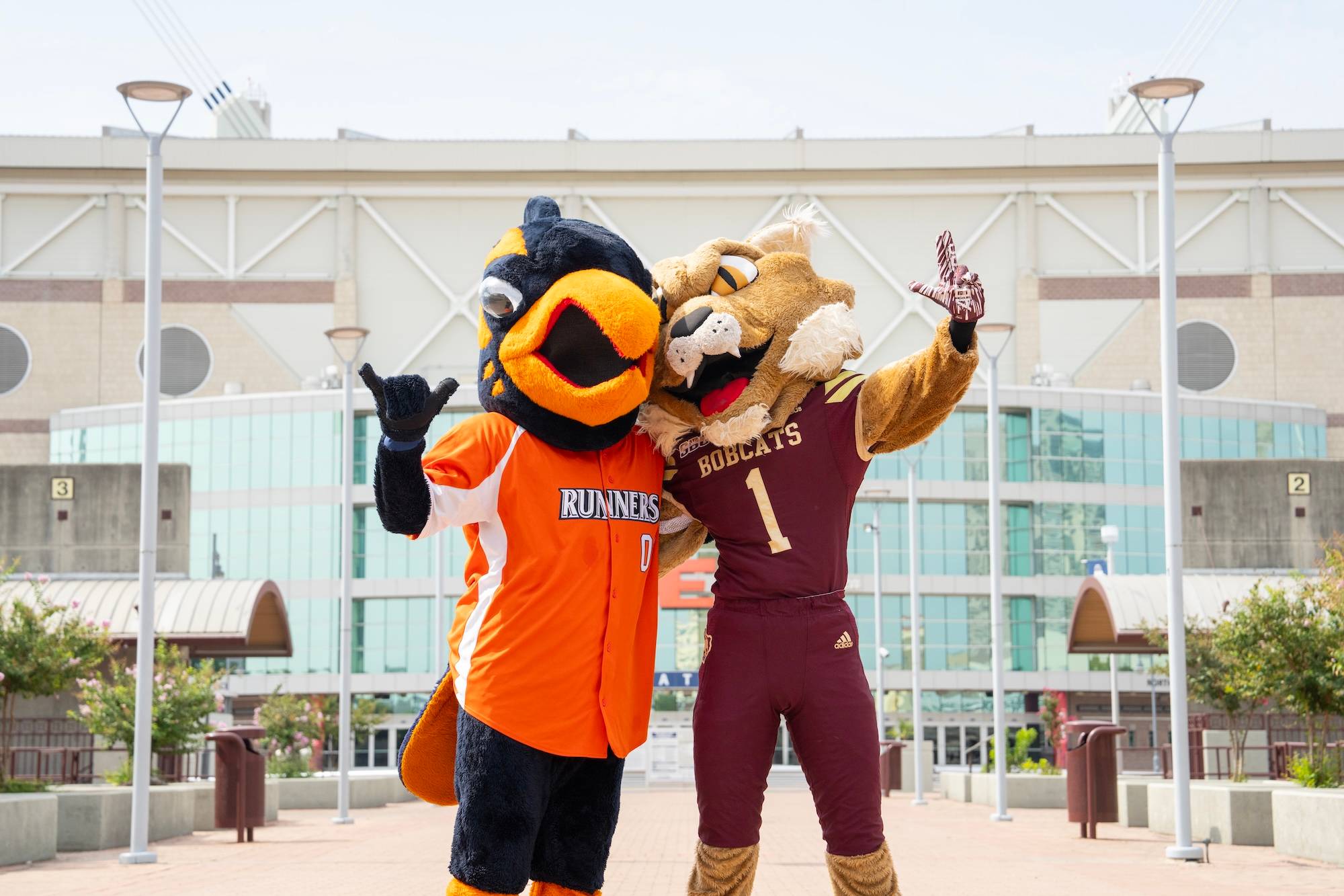 roadrunner and bobcat mascot pose for photo together in front of large football stadium