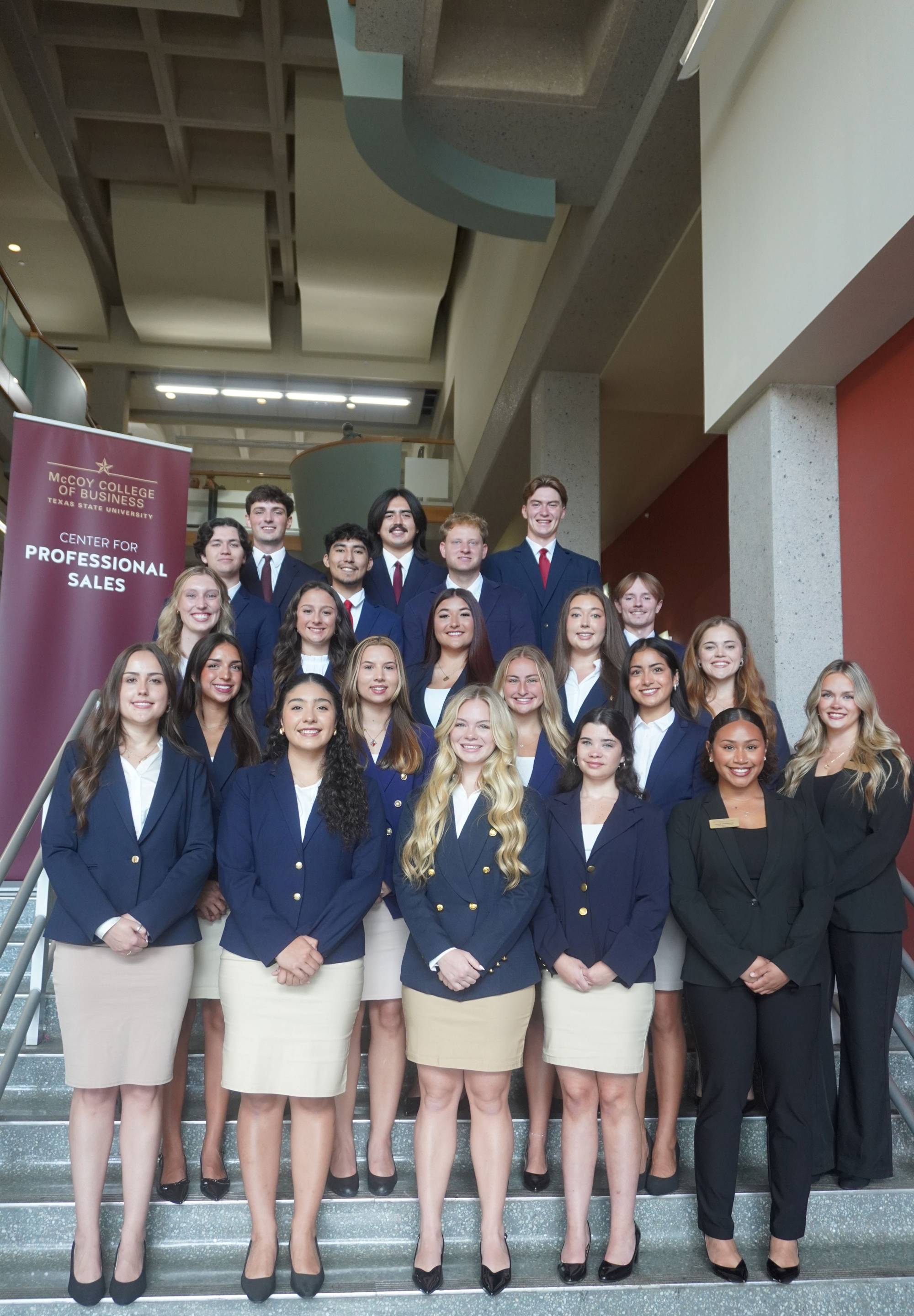 Group of Sales Ambassadors standing on the stair case in khaki bottoms and navy blue suits.